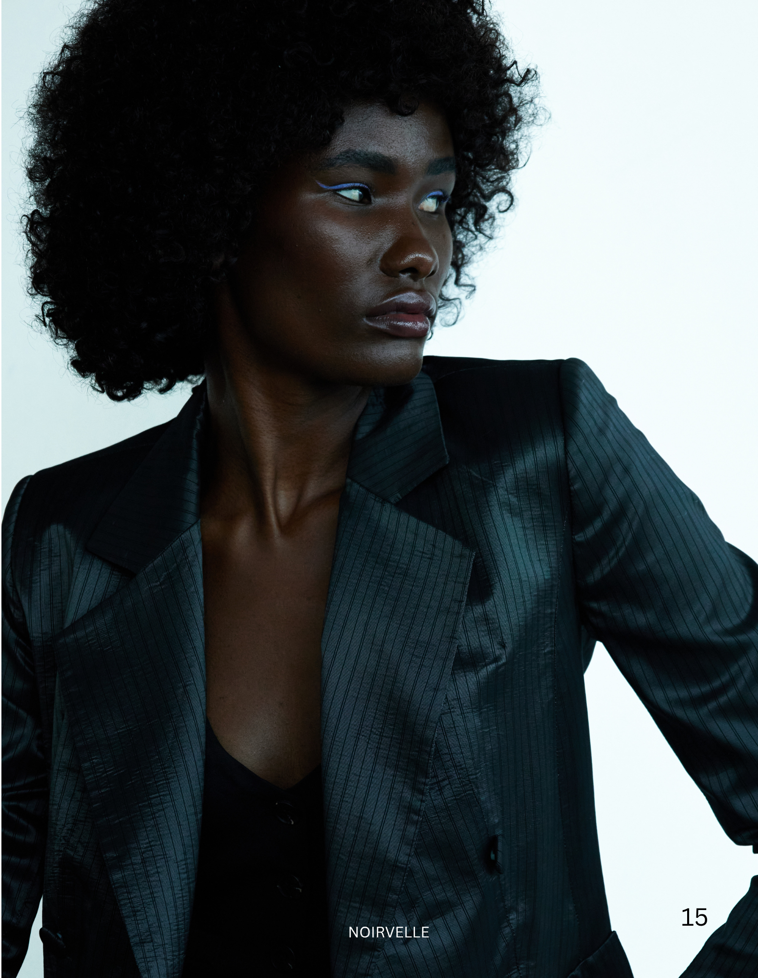 Fashion portrait of a female model with curly black hair wearing a pinstripe blazer, photographed by Noirvellel.