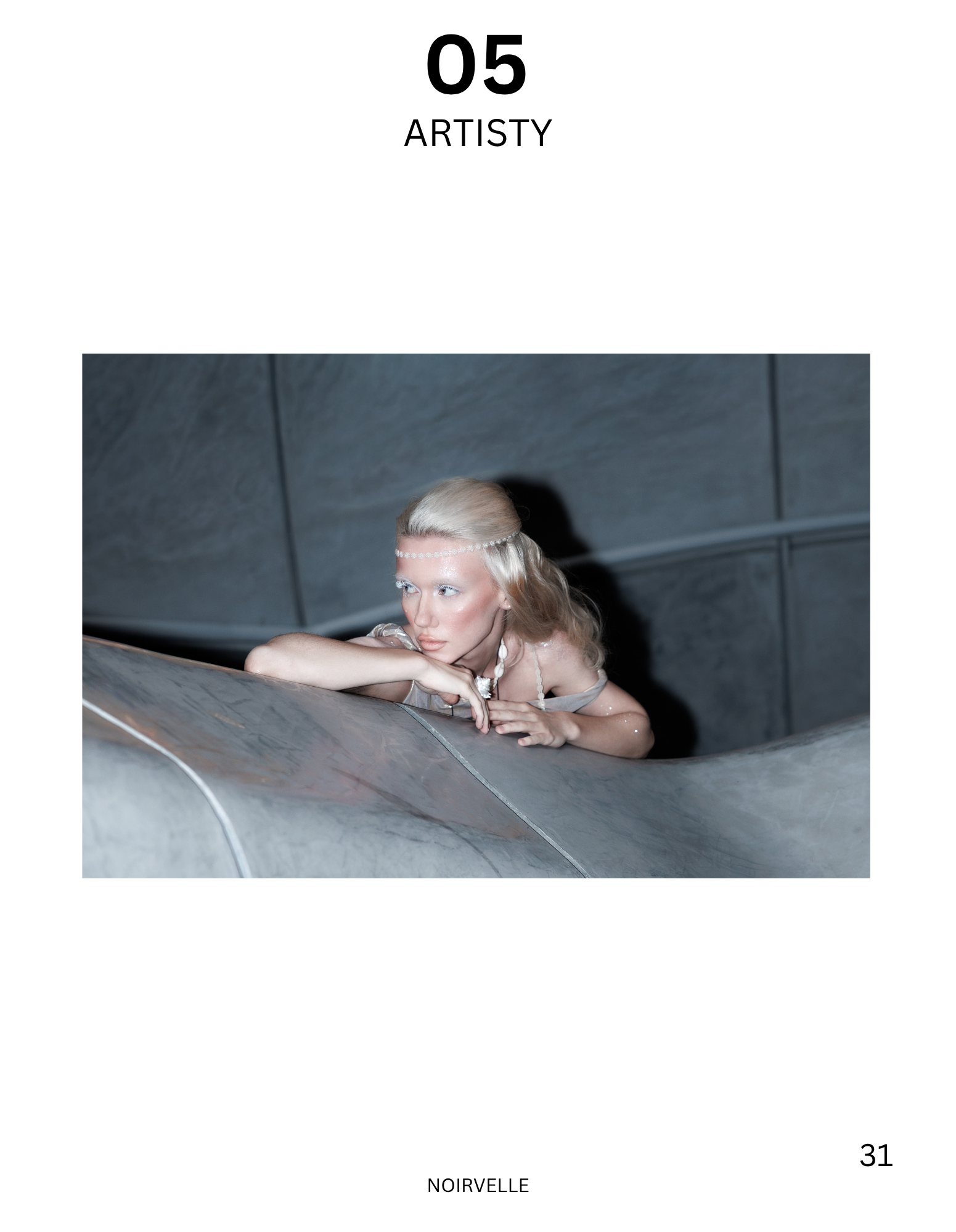 A woman with platinum blonde hair and fair skin resting her head on her arm on a metal surface in a dimly lit setting with a dark gray ceiling in the background.