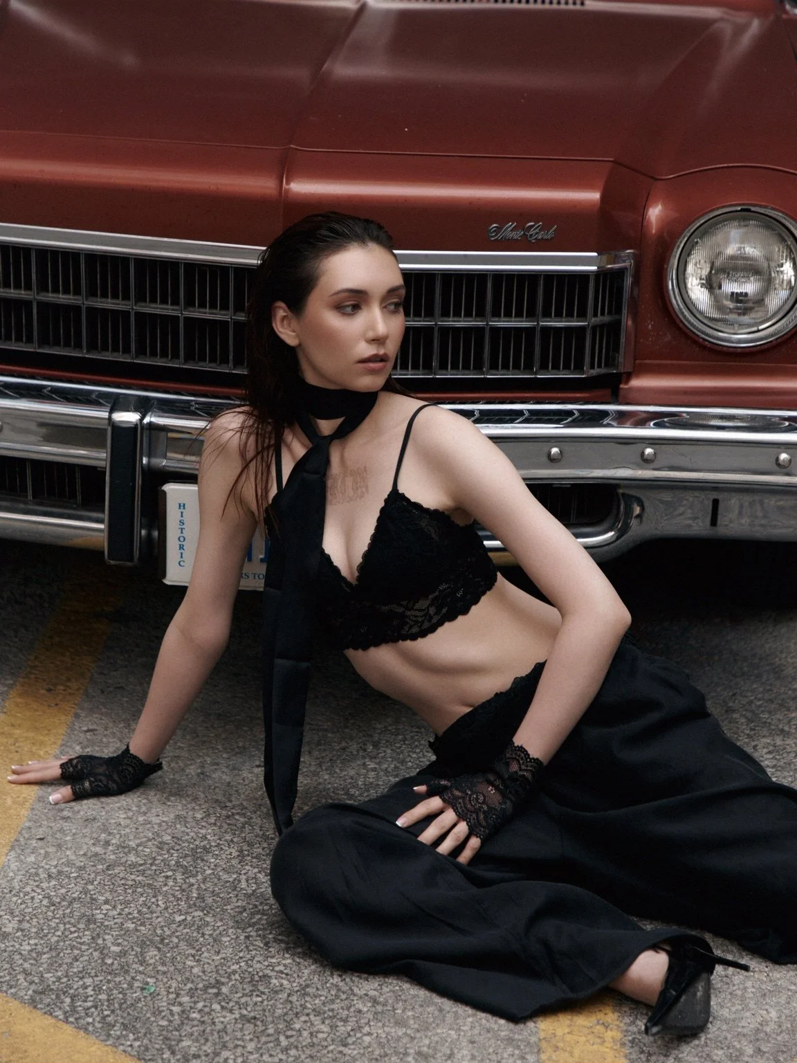 Professional fashion model in a black editorial look posing beside a vintage car – Noirvellel

