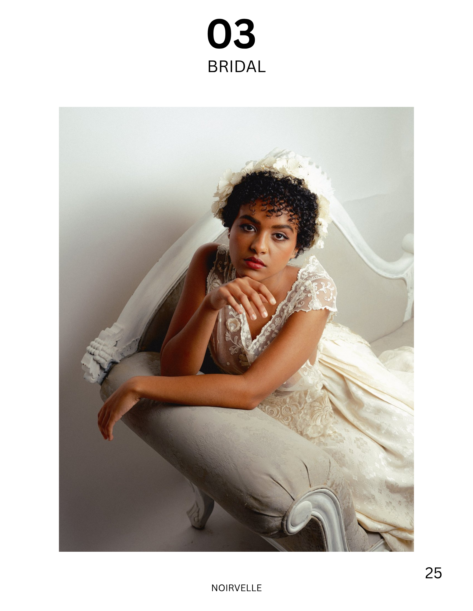 Portrait of a woman with short curly dark hair, wearing a white lace dress and a floral headpiece, sitting on an ornate white antique chaise lounge, looking directly at the camera.