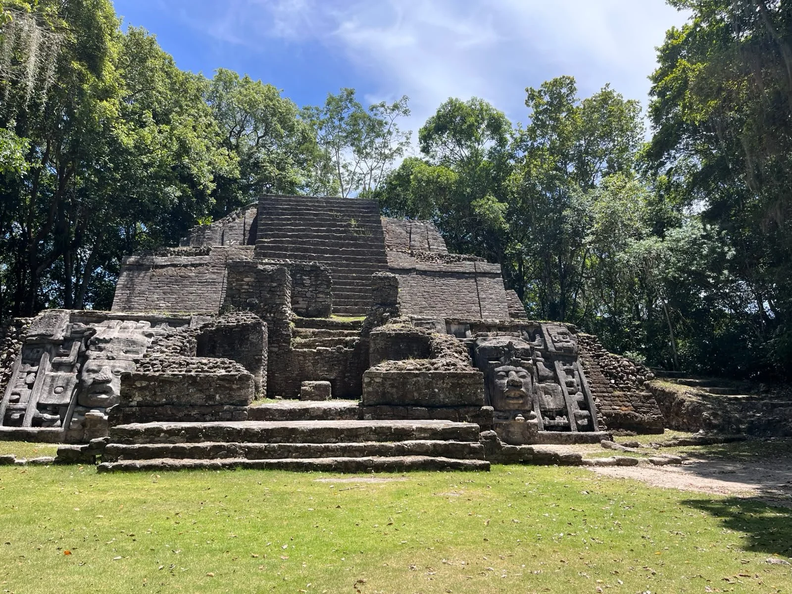 Ancient stone step pyramid surrounded by lush green trees with a clear blue sky in the background.