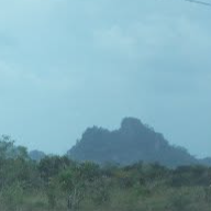 A distant view of a hill or small mountain with lush green vegetation under a cloudy sky.