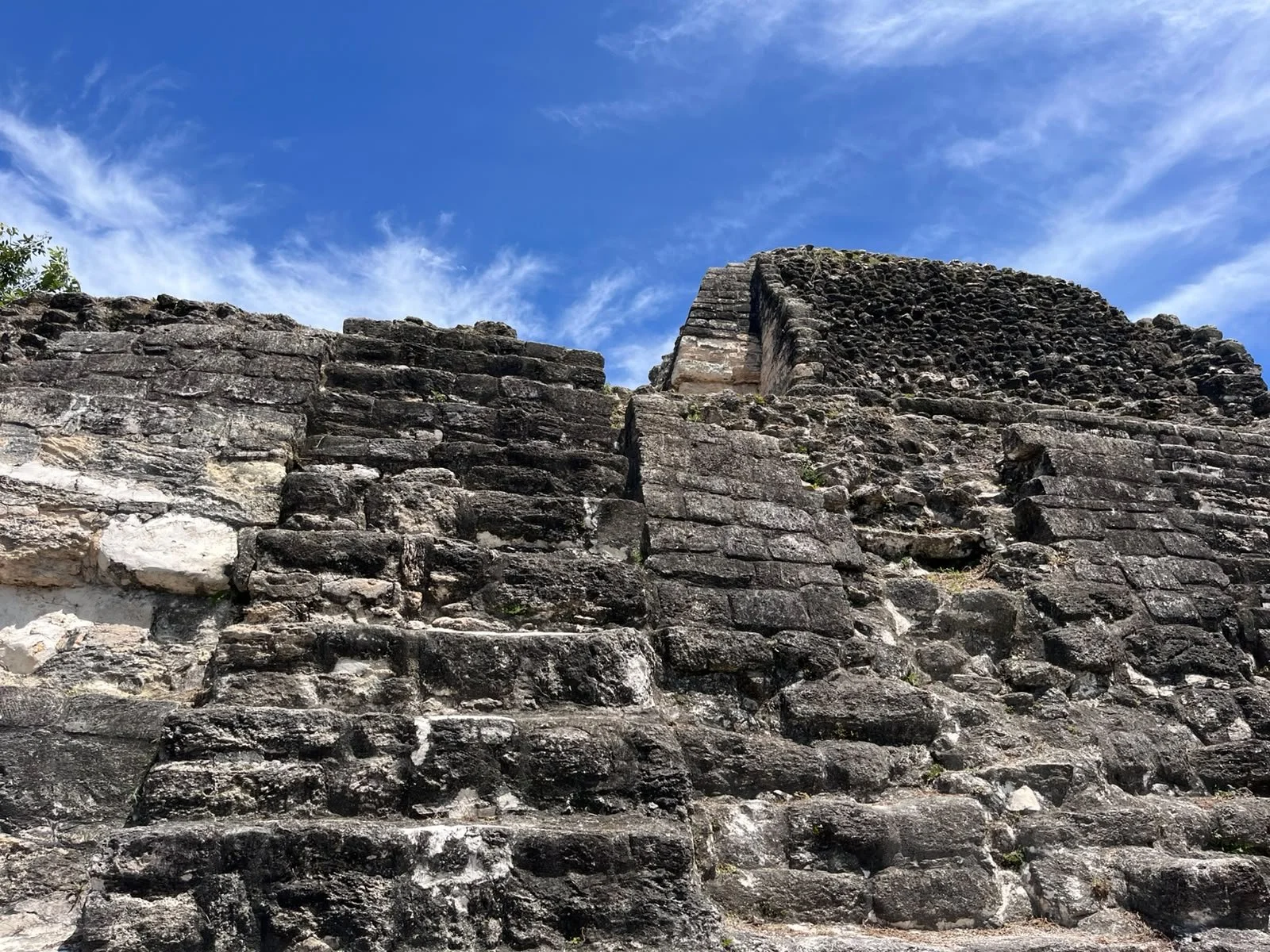 Ancient stone step pyramid against a bright blue sky with wispy clouds.