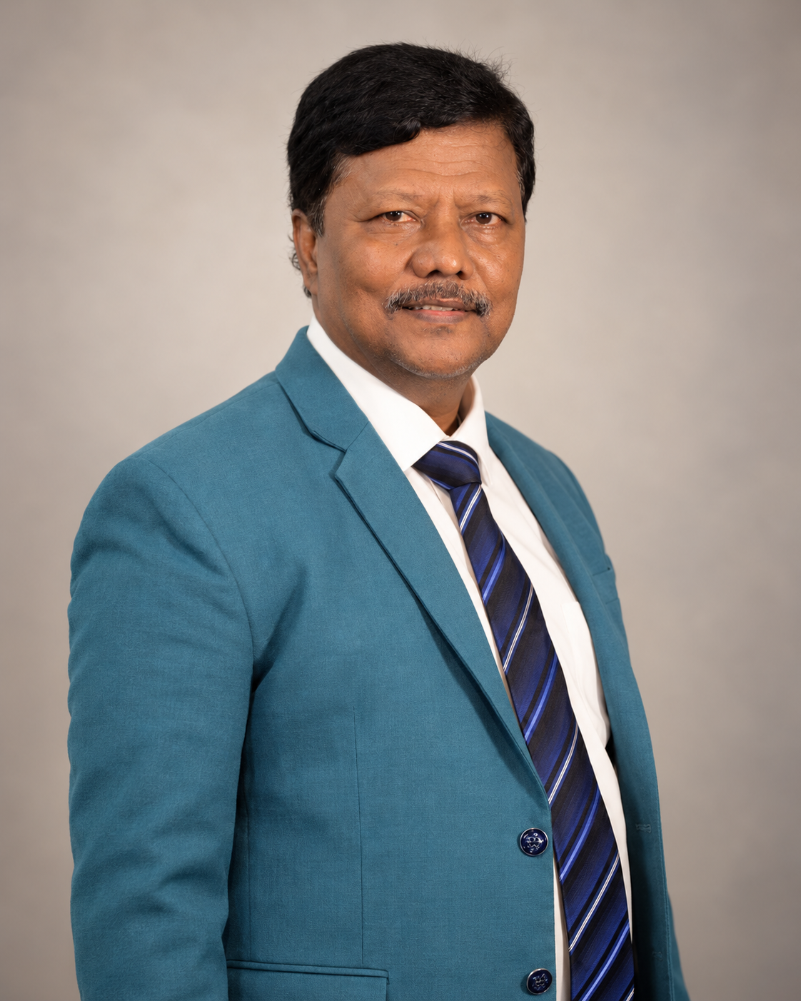 A middle-aged man with dark hair and a mustache, wearing a teal suit, white shirt, and a striped blue tie, standing against a neutral background.