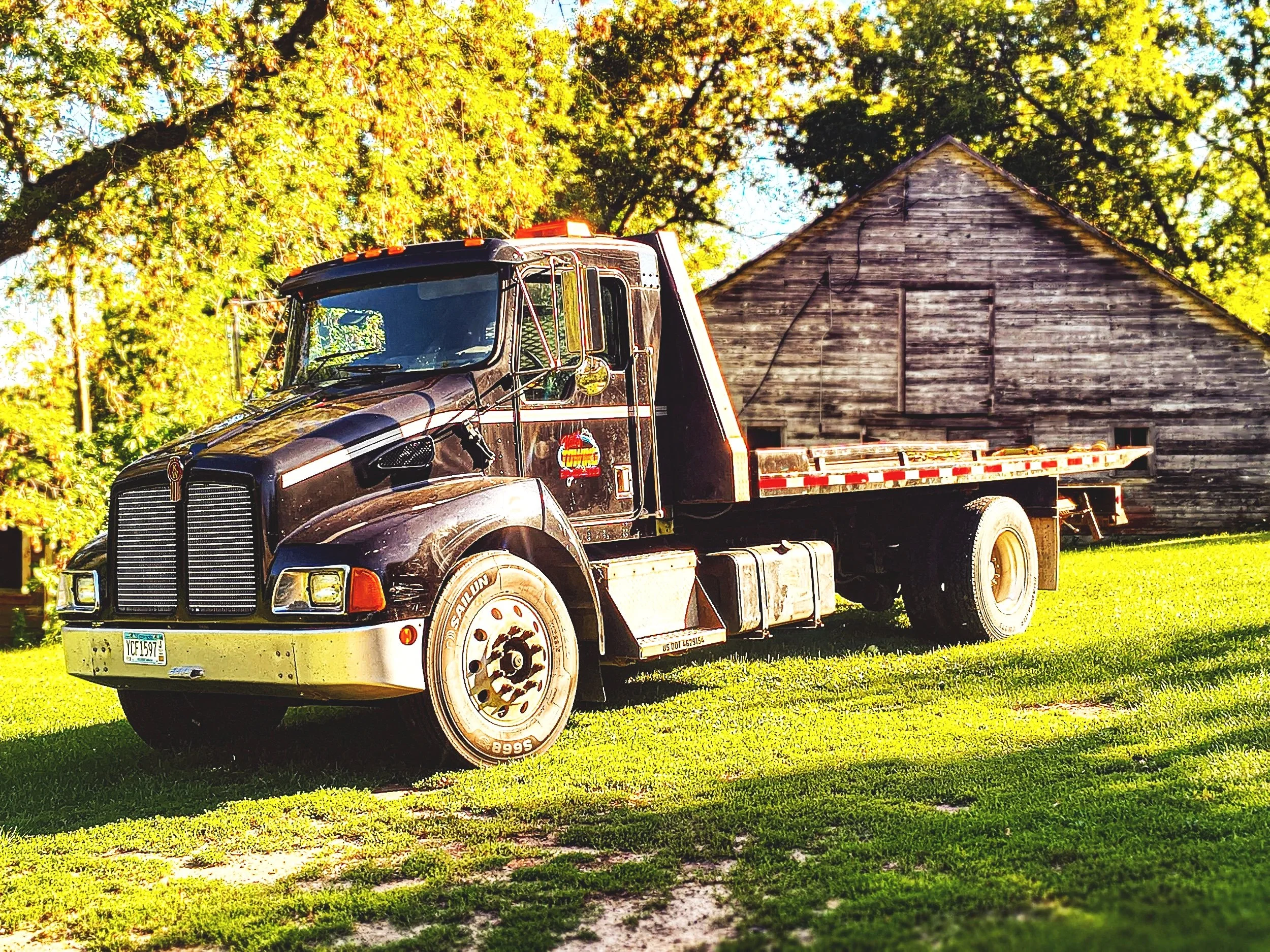 A black flatbed truck parked on a grassy area with green grass, yellow trees, and a wooden barn in the background.