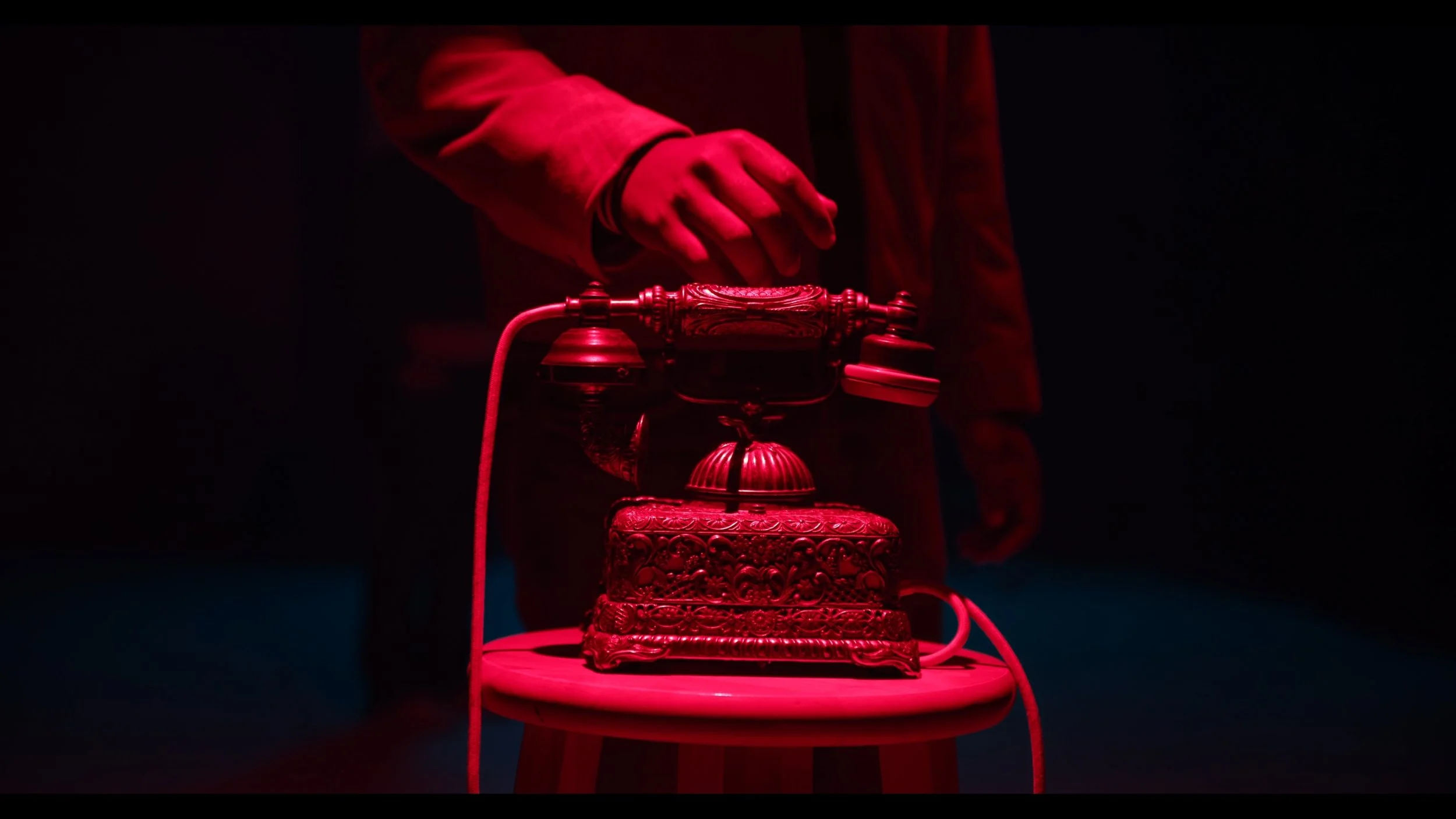 A hand reaching for an antique telephone under vivid red light in Telephone Man.