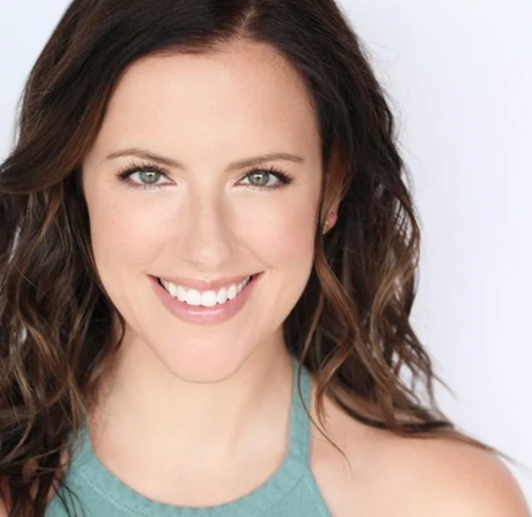 Close-up portrait of a smiling woman with wavy brown hair, light skin, and green eyes, wearing a teal sleeveless top.