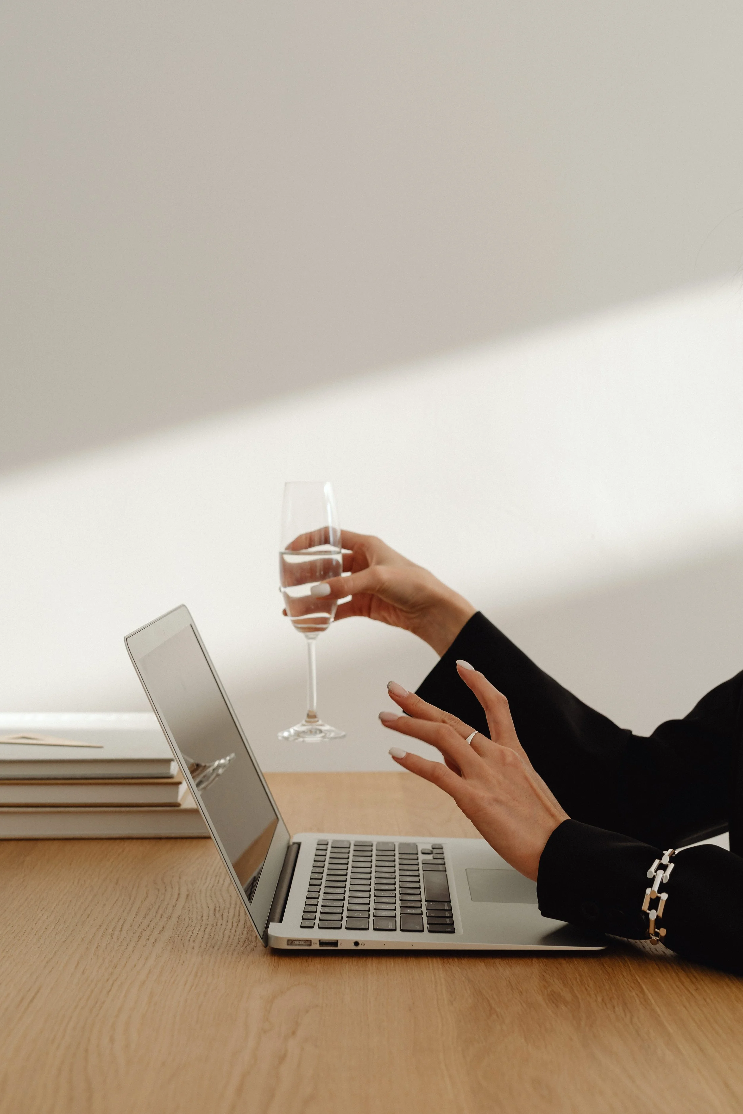 Una persona sorseggia un bicchiere di acqua mentre lavora su un laptop accanto a un tablet e alcuni quaderni, in un ambiente minimalista e ben illuminato.