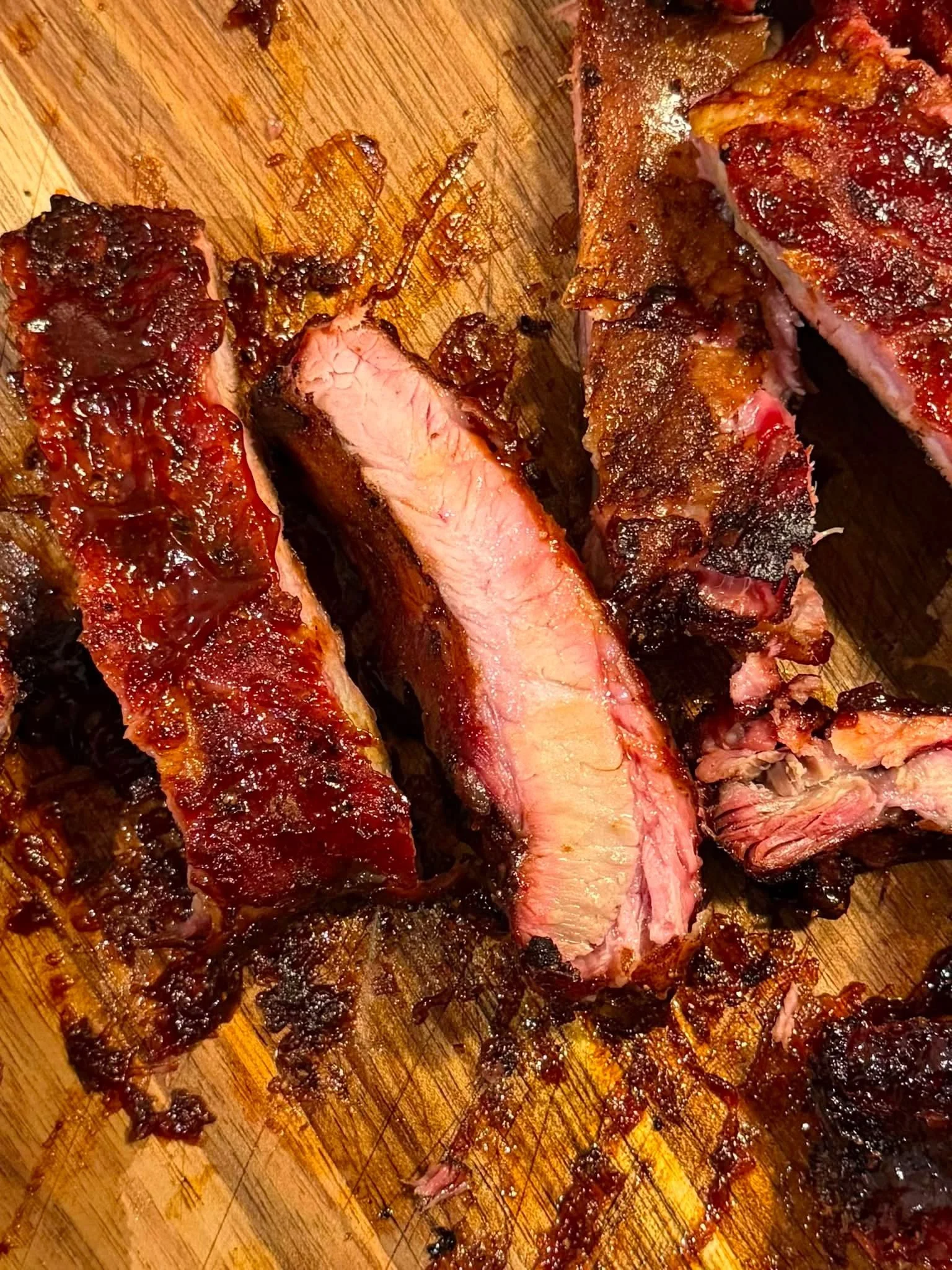 Close-up of grilled ribs on a wooden cutting board, showing a charred exterior and tender pink meat inside.