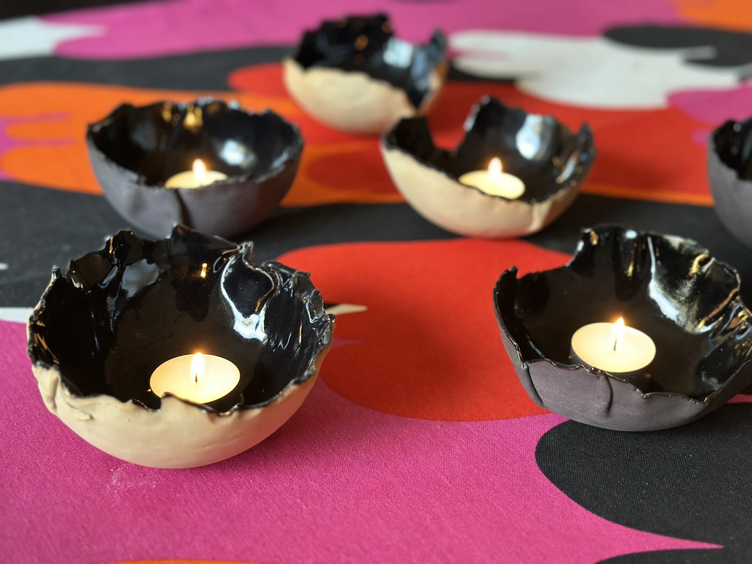 Decorative tealight candles in black shells arranged on a black and pink patterned surface.