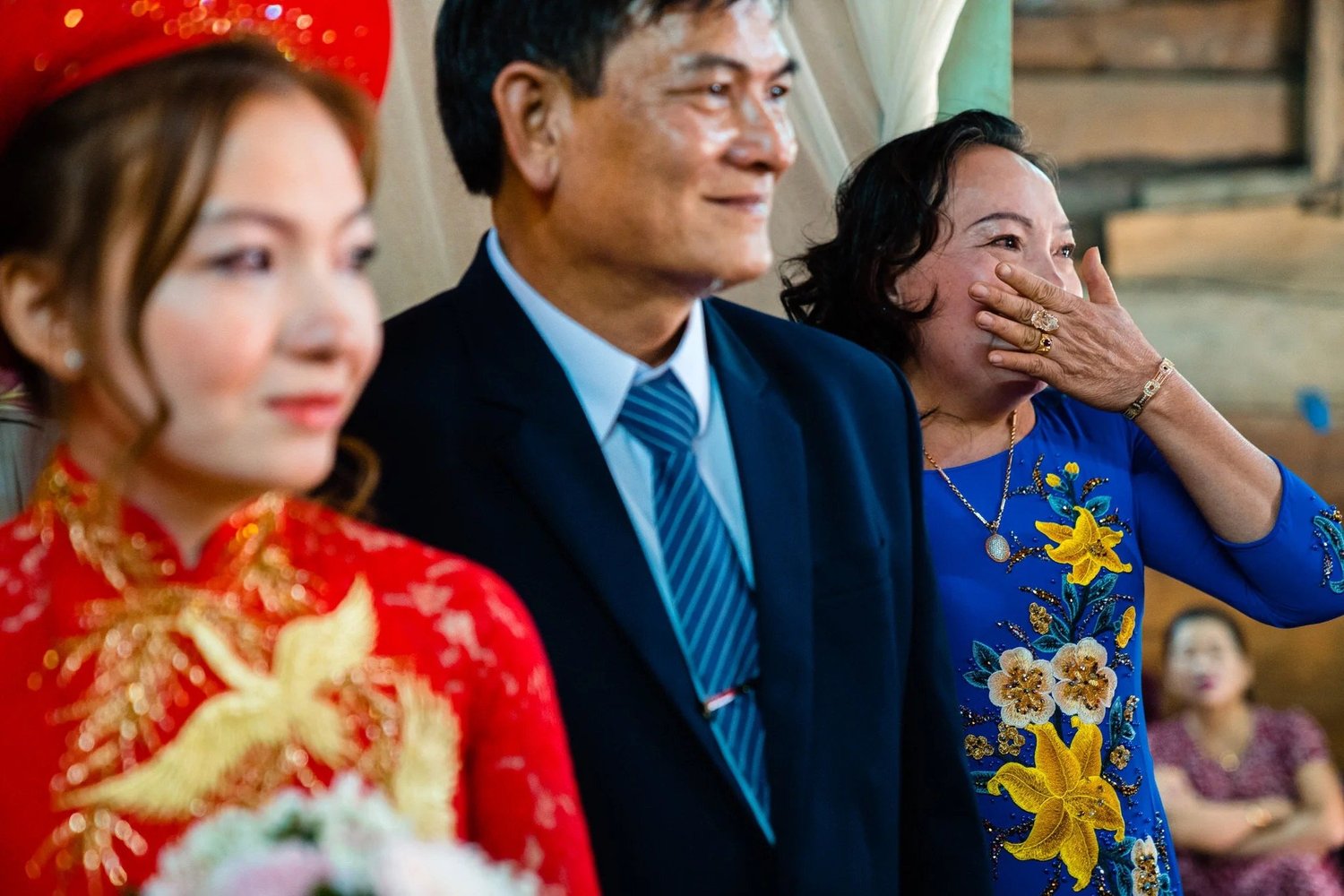 A woman in blue covers her mouth beside the bride and a man during Minh and Hanh’s ceremony