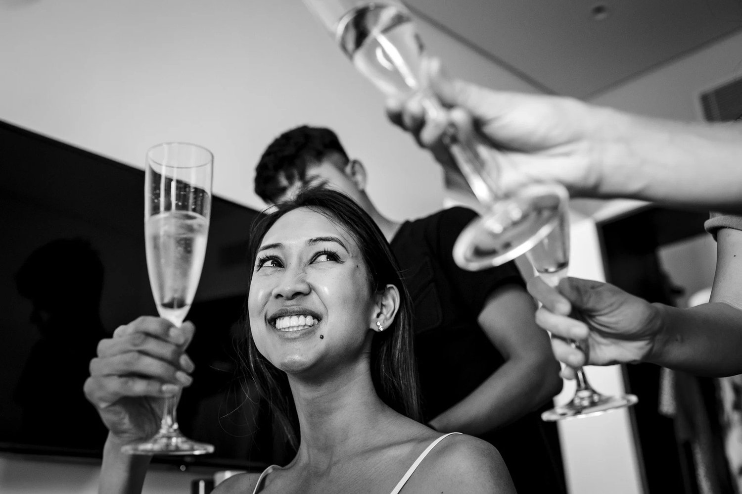 The bride smiles during preparations, surrounded by people helping her.