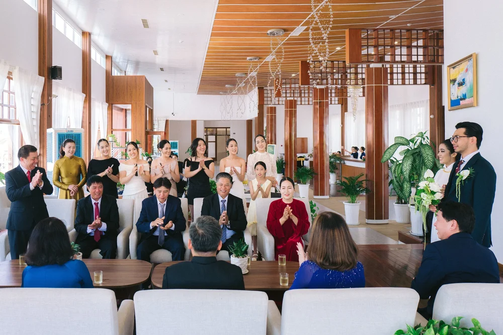 A wider view of the gathering clapping, with the smiling couple at the right