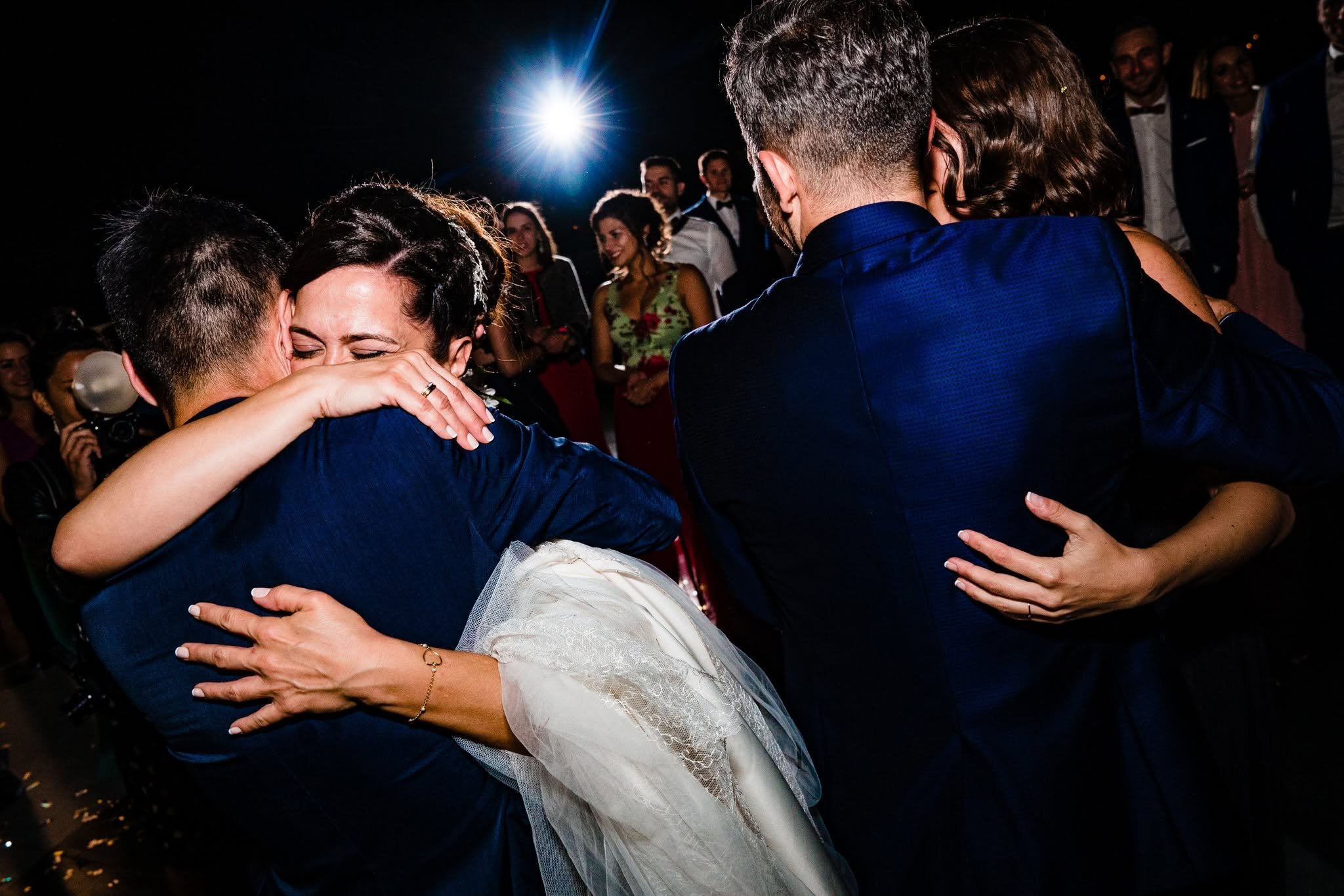 Ana embraces a guest tightly while another pair embrace beside them at her wedding in Ponferrada.