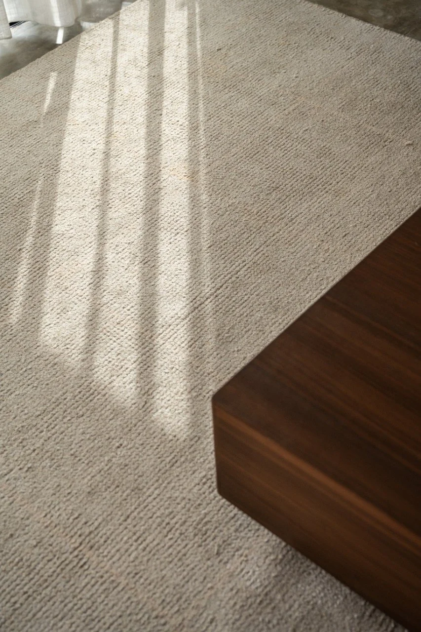 Part of a beige carpet with shadows cast from a nearby window and a wooden table corner.