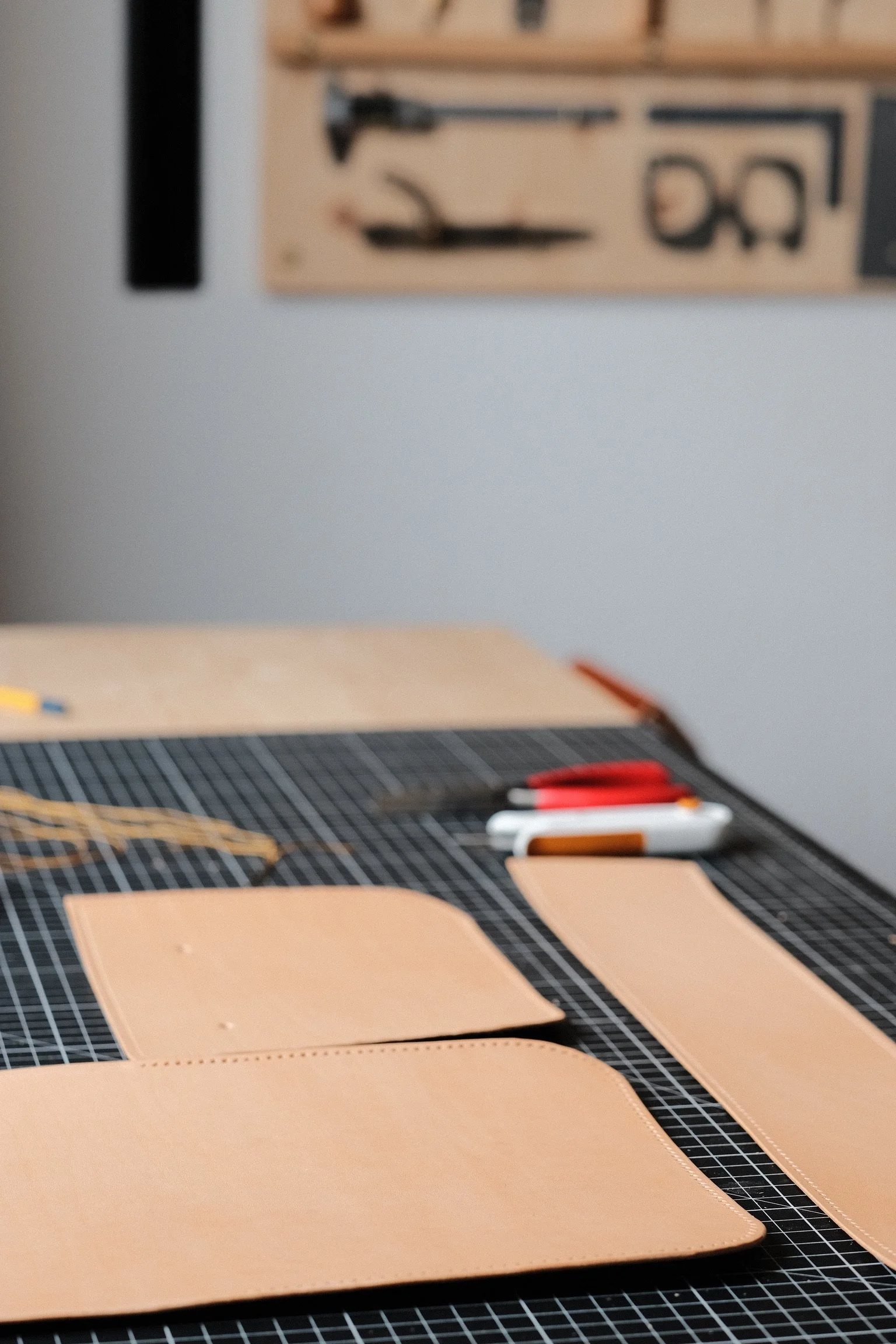 Leather crafting tools and materials on a workbench, including pieces of leather, threading, and cutting tools.