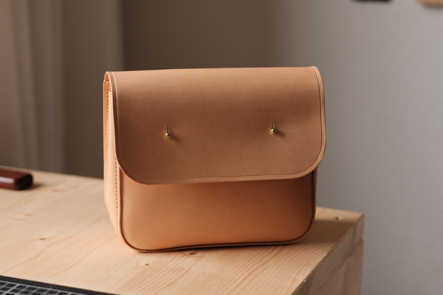 A tan leather handbag on a light wooden table with a plain wall in the background.