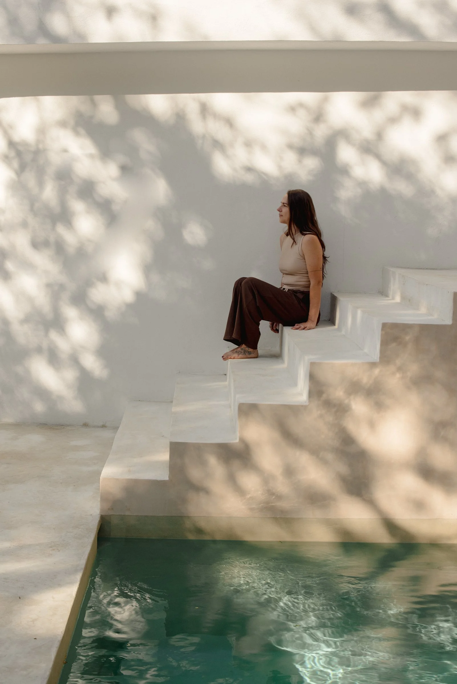 Larissa Van de Bilt sitting on sunlit white stairs above a pool