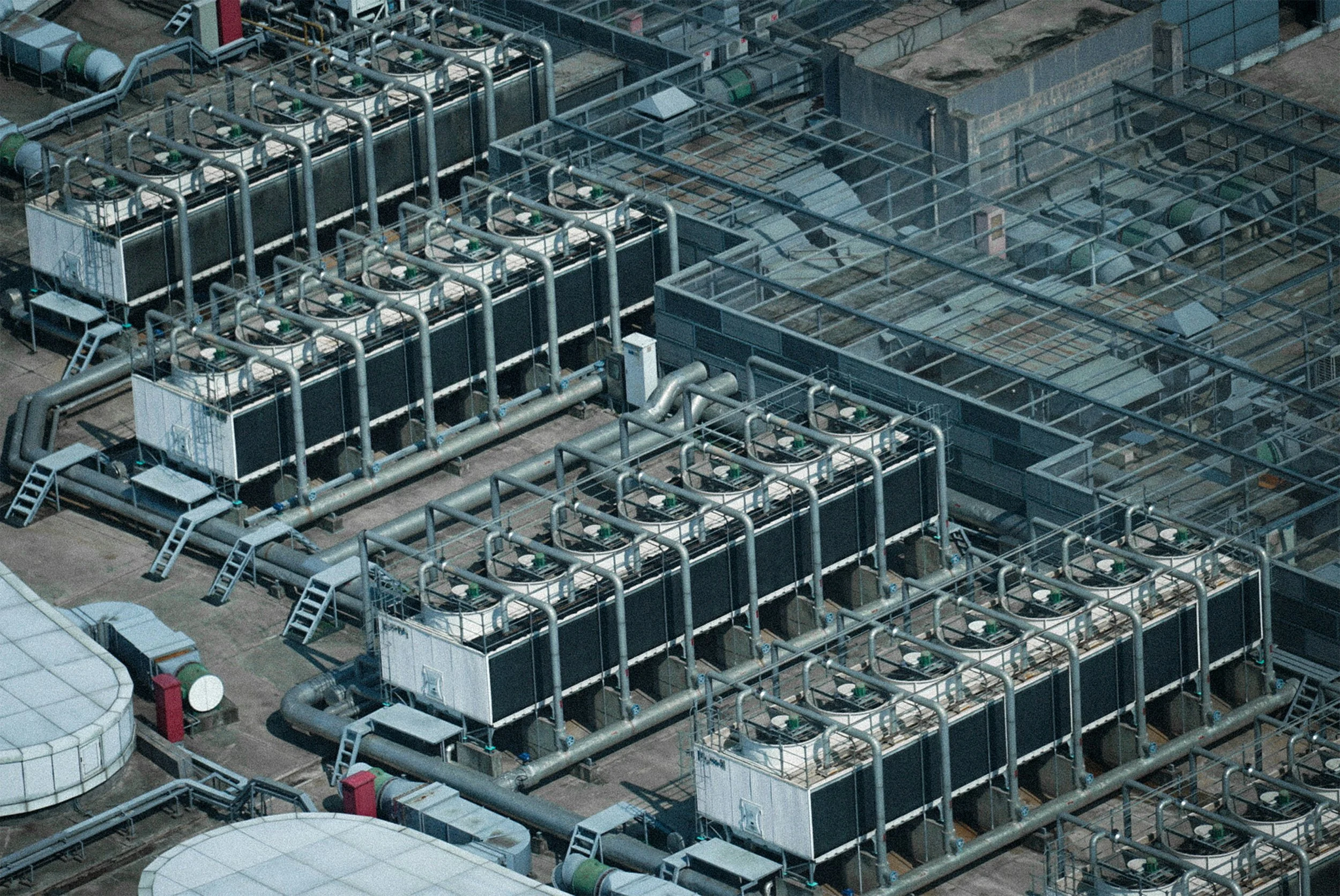 An aerial view of an industrial rooftop showing multiple HVAC units and interconnected metal pipes.