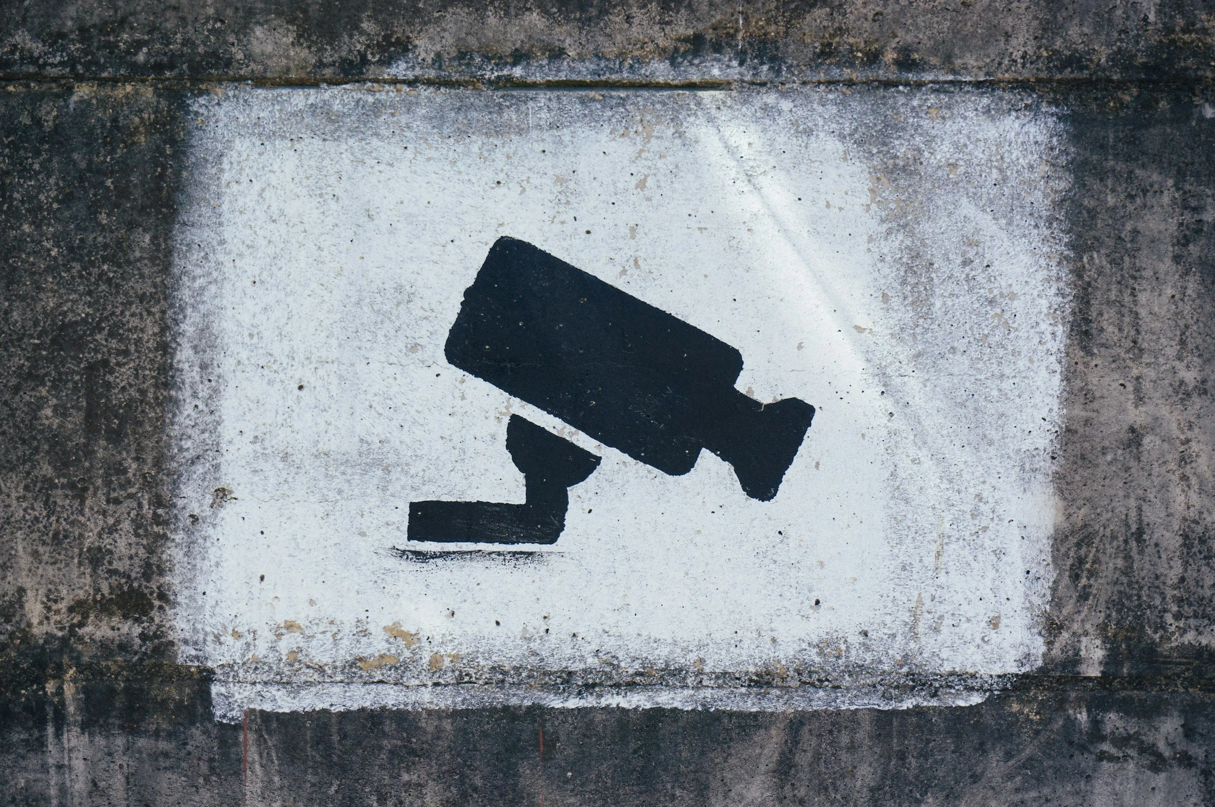 Graffiti of a black spray-painted security camera on a concrete wall.