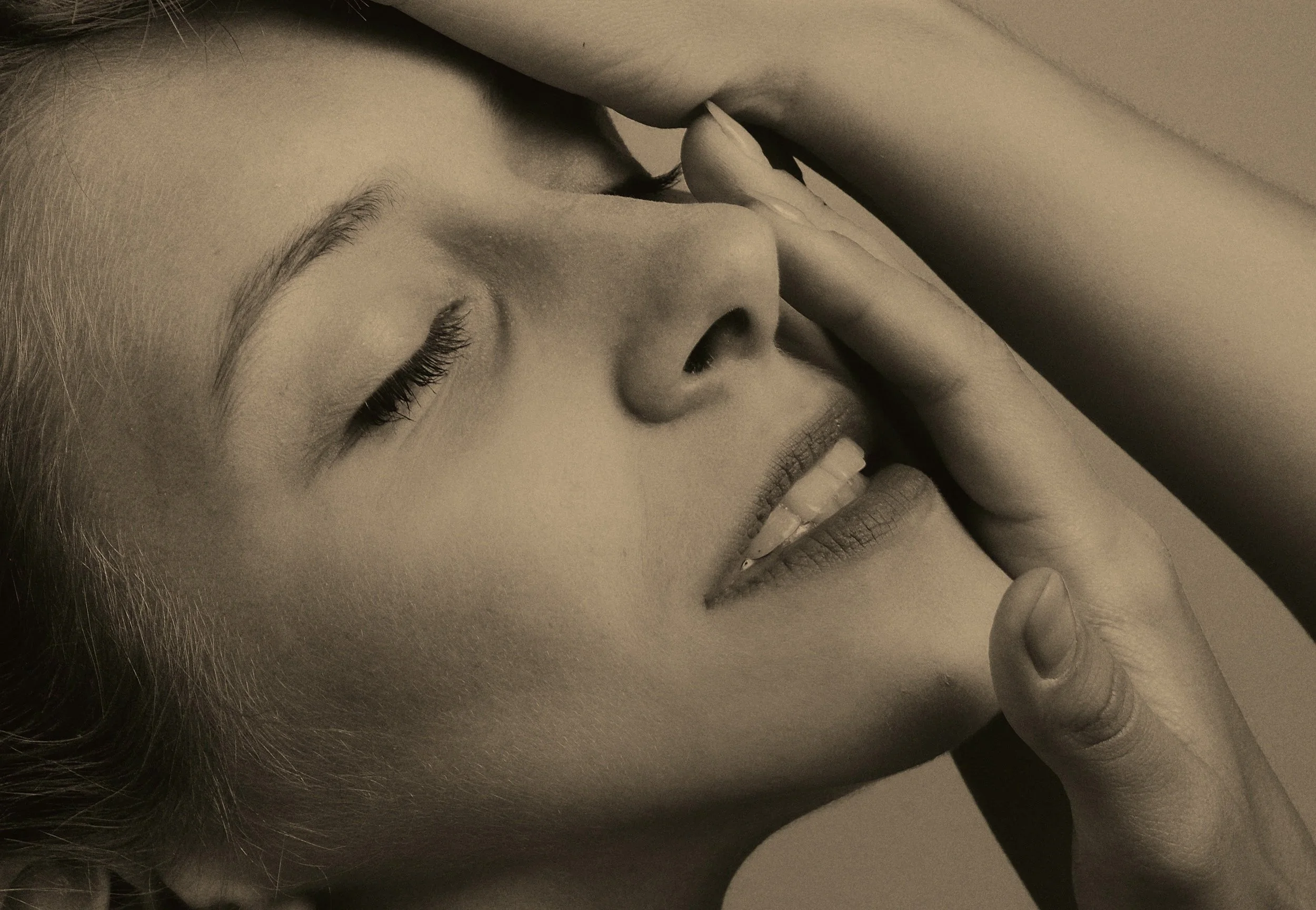A close-up black and white photo of a woman's face with her eyes closed and fingers touching her lips.