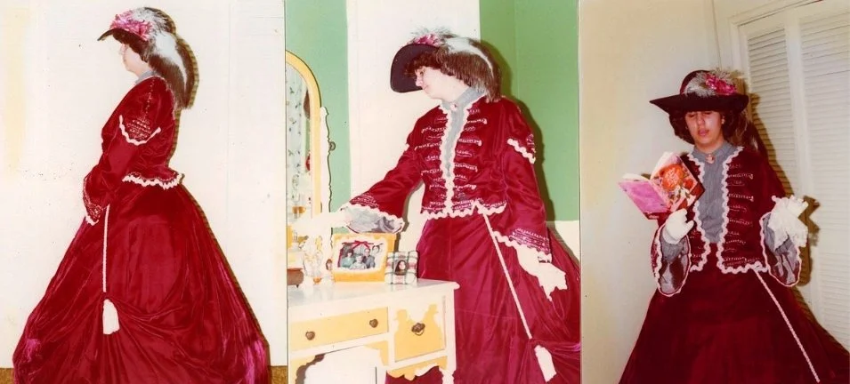 Three women dressed in Victorian-style red and black dresses with hats, reading books and standing in a vintage room.