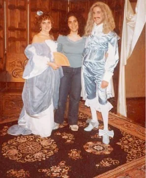 Three women in costume standing together indoors on a patterned carpet.
