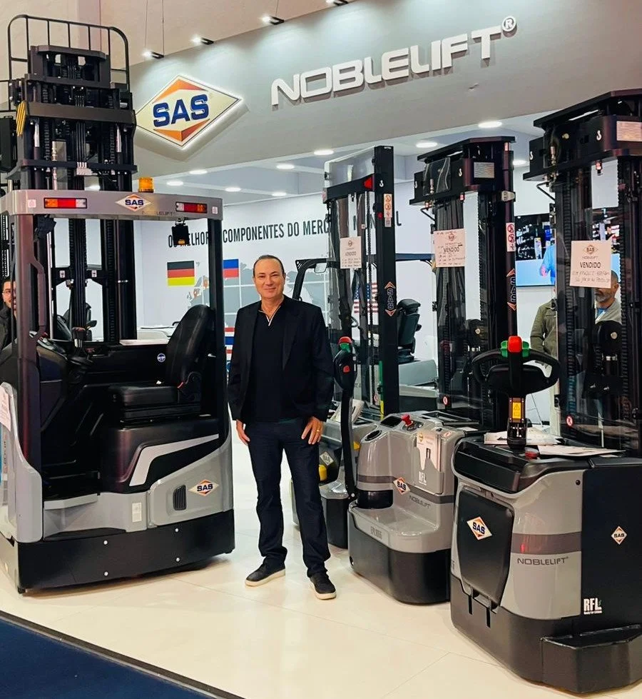 A man standing in front of several forklifts at a trade show booth with the brand name 'NOBLELIFT' and the logo 'SAS' displayed above.