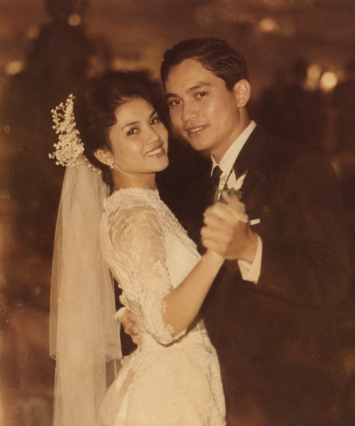A vintage wedding photo of a bride and groom dancing together, dressed in traditional wedding attire, smiling and looking at the camera.