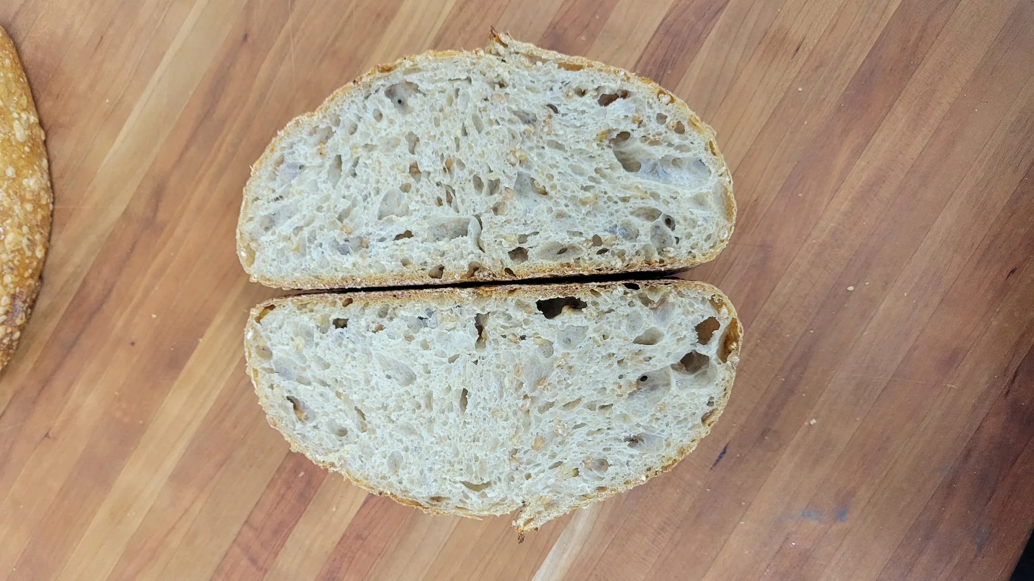 A sourdough loaf cut in half on a wooden board, showing its airy crumb and golden crust.