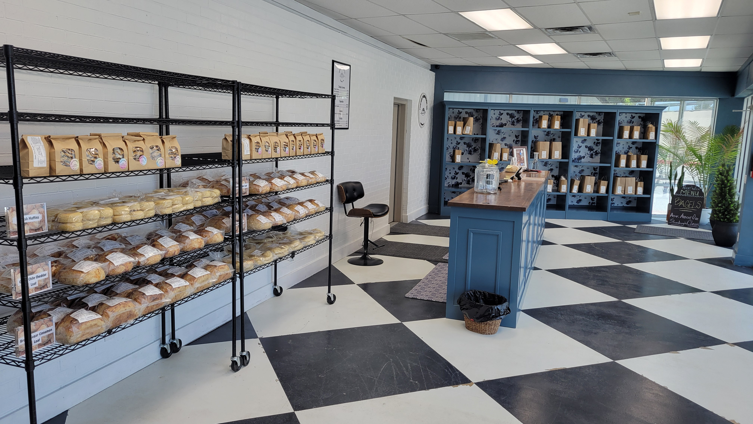 Bread and baked goods displayed on shelves inside The Bread Box, with a blue counter and black-and-white tiled floor.