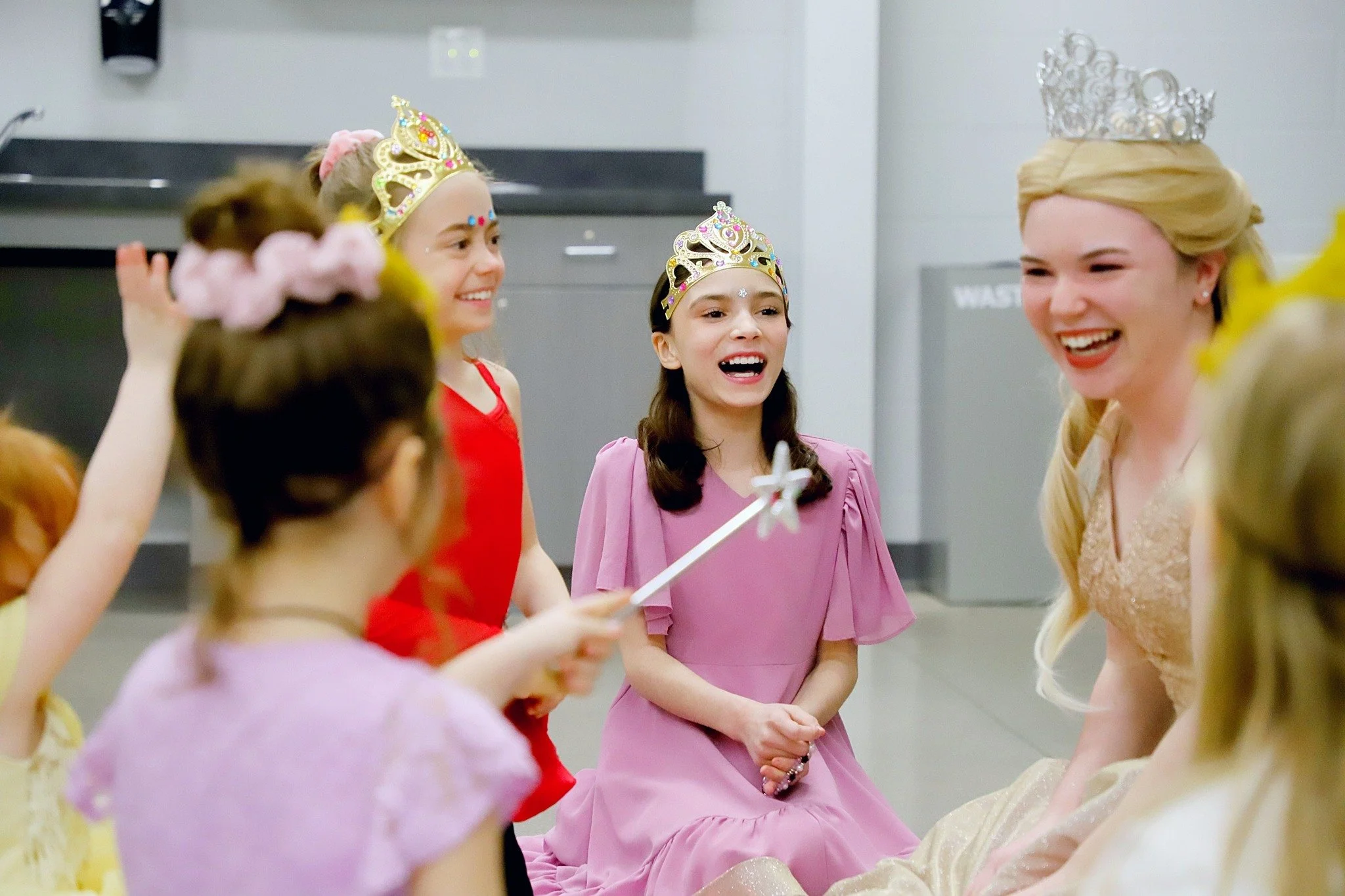 A group of children and an adult woman, all wearing crowns, smiling and interacting at a party or celebration.