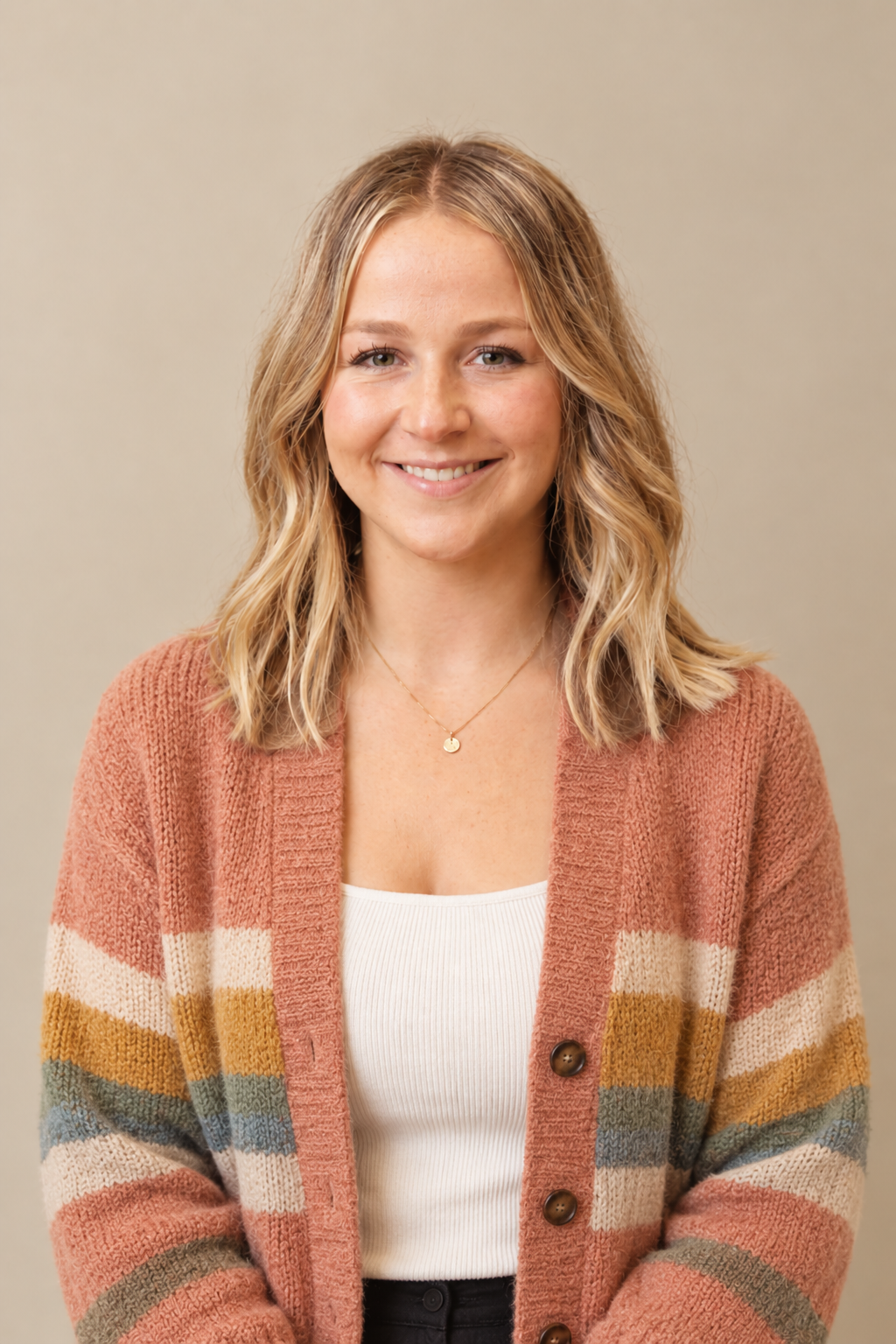 Smiling woman with wavy blonde hair wearing a striped, multicolored cardigan and a white top.