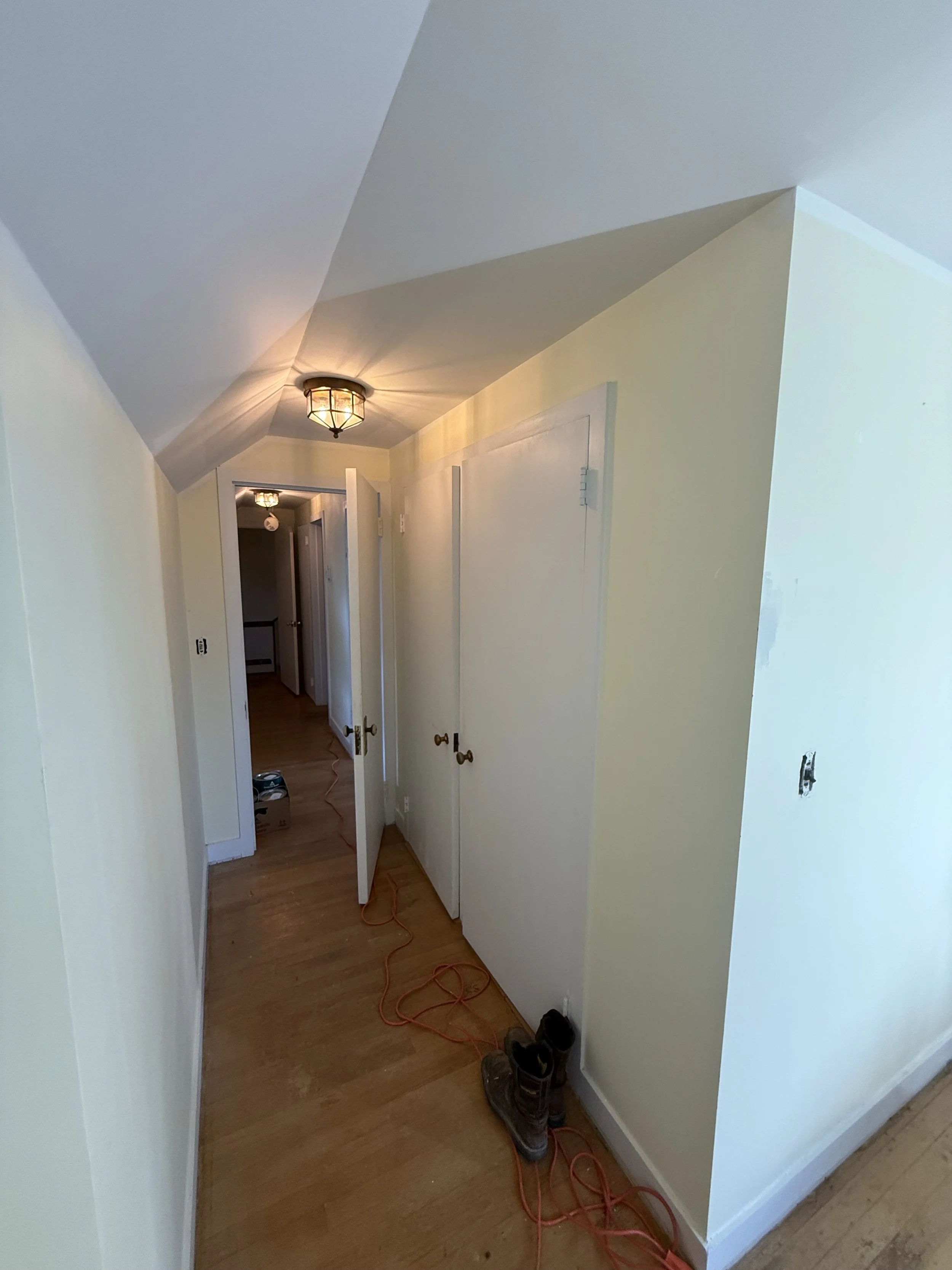A hallway in a house undergoing renovation with open closet doors, construction tools, and shoes on the floor.