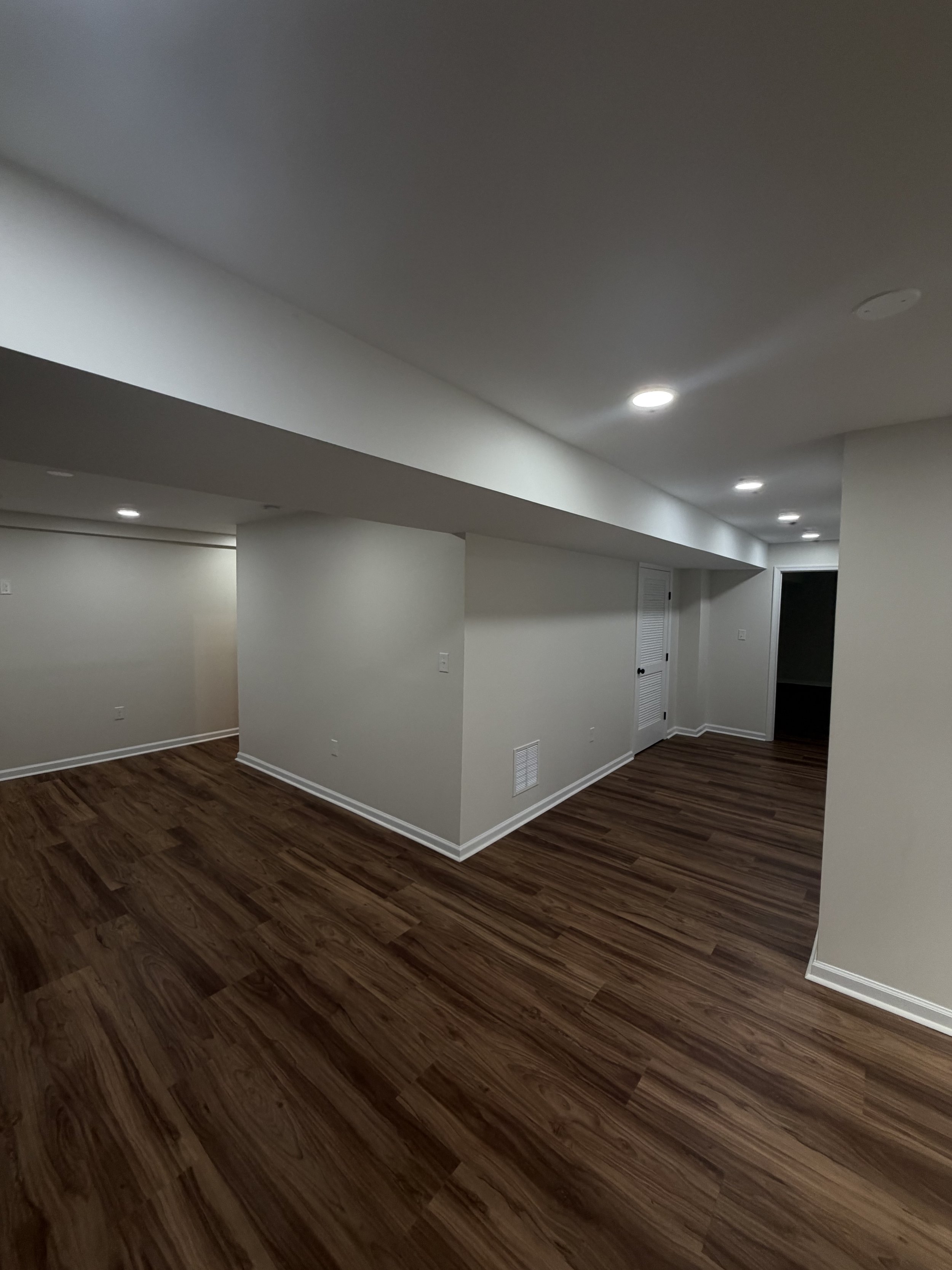 Empty room with white walls, wood flooring, and ceiling lights.