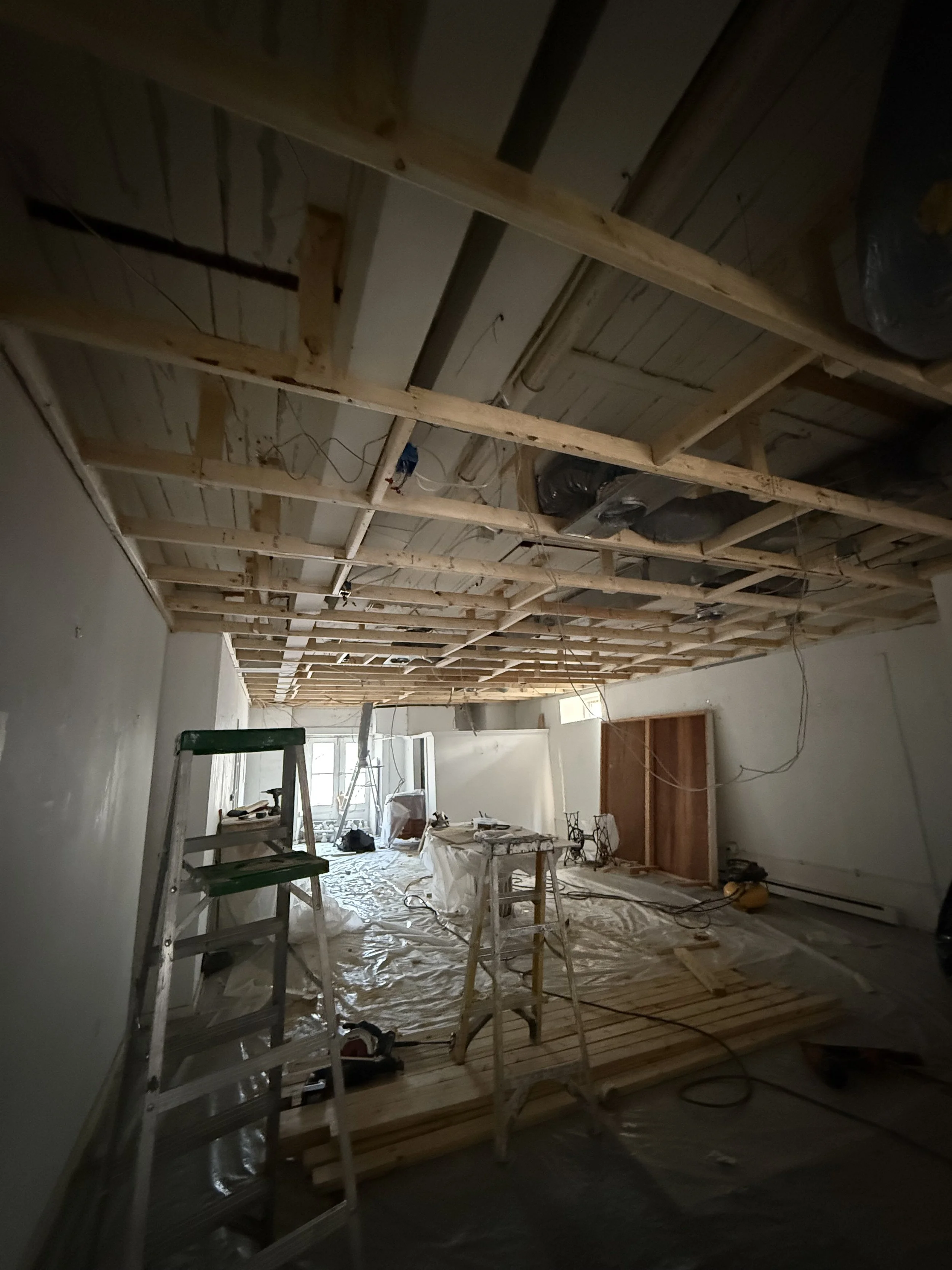 A room under construction with exposed wooden framing on the ceiling and various tools and equipment scattered around.