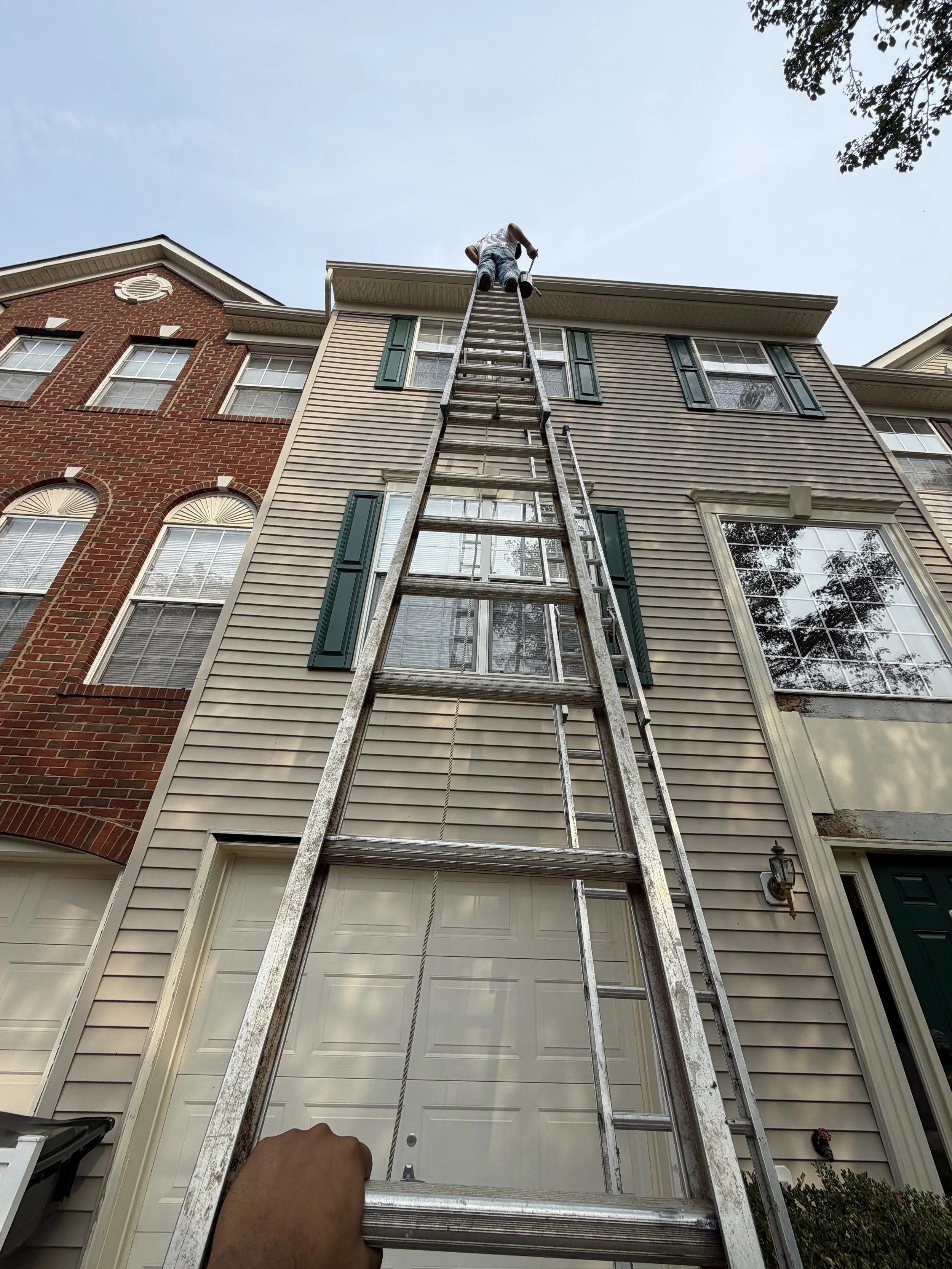 Person on a ladder installing or repairing the eaves on the roof of a suburban house.