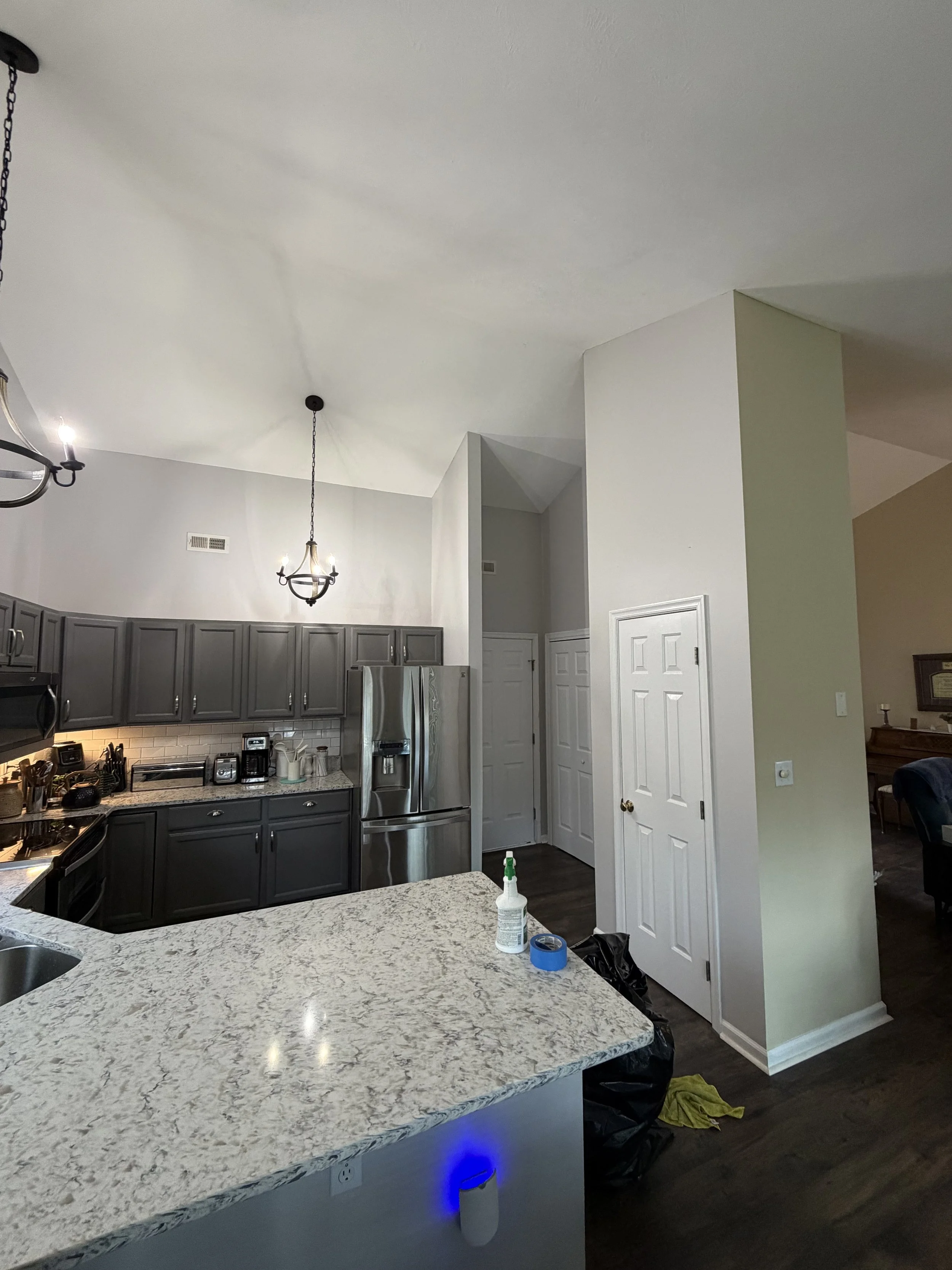 Kitchen with white and gray cabinets, stainless steel refrigerator, granite countertops, pendant lights, and a circular chandelier.
