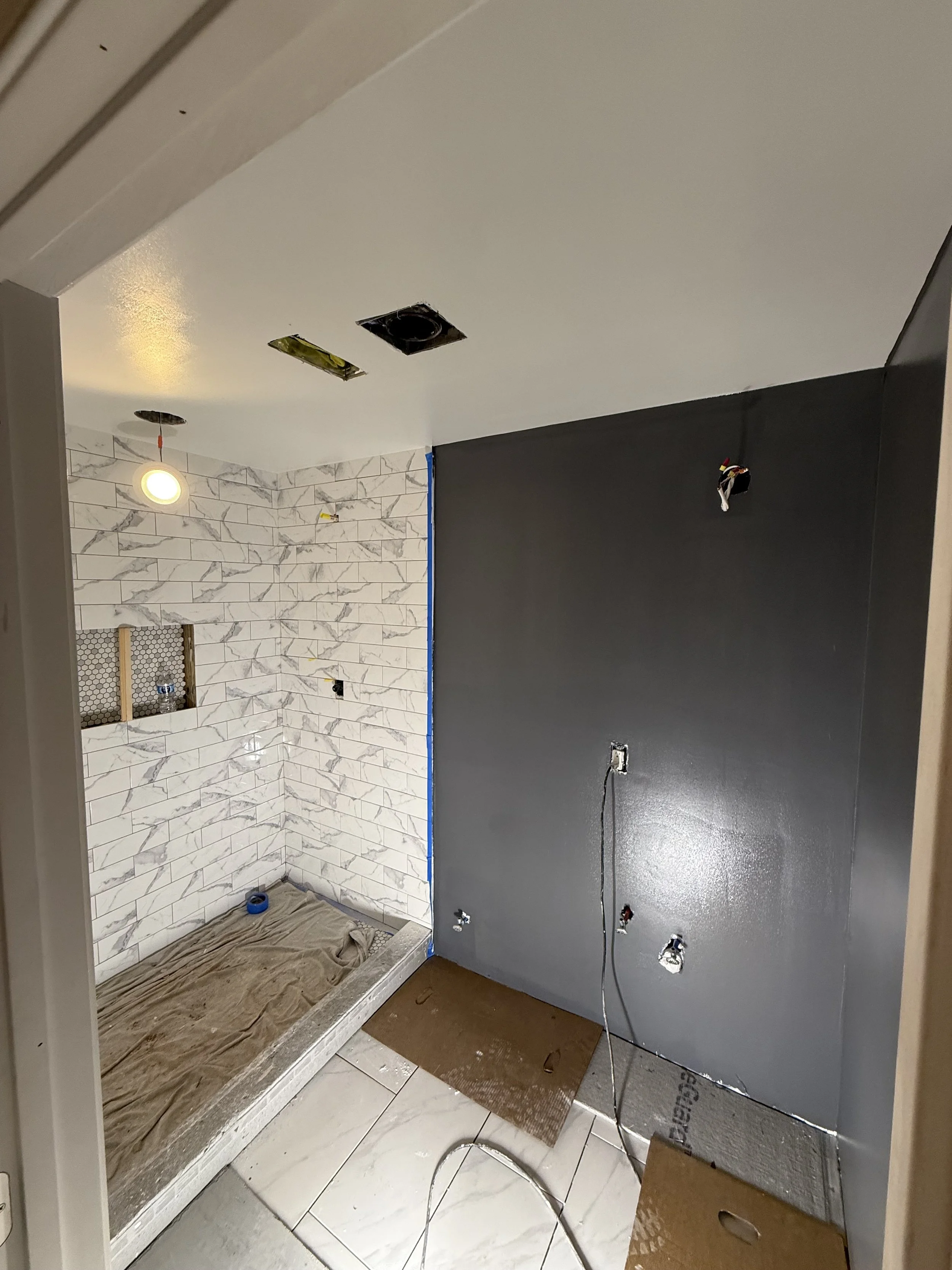 Bathroom renovation with tiled wall, unmounted light fixture, and construction materials.