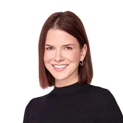 A woman with shoulder-length brown hair, smiling, wearing a black top, against a white background.