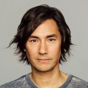 Headshot of a man with medium-length dark hair and a neutral expression, wearing a gray shirt.