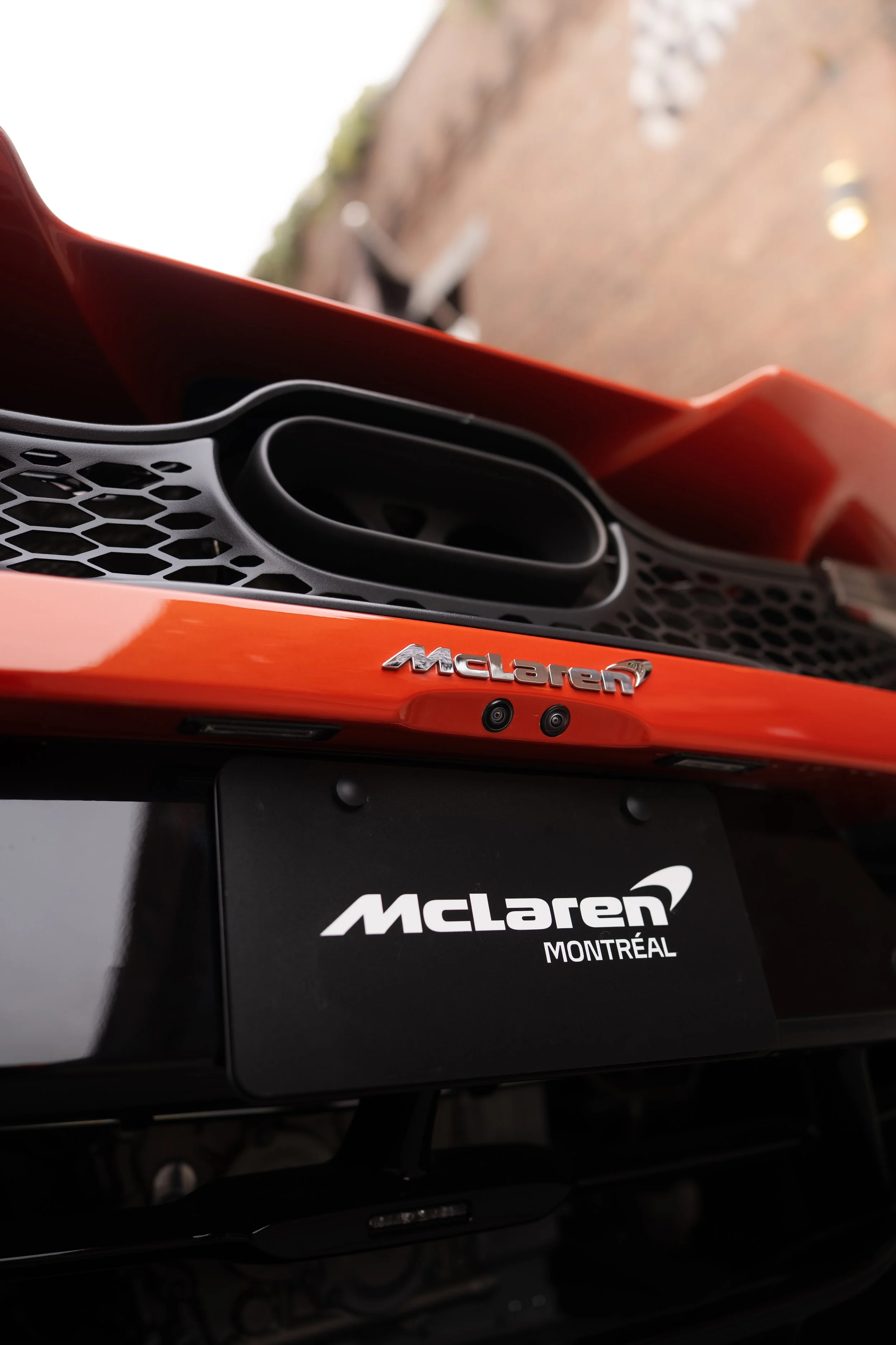Close-up of a McLaren car front grille with the McLaren badge, showing sleek red bodywork and black accents.