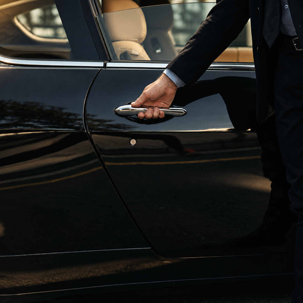 A person in a black suit opening the door of a black luxury car.