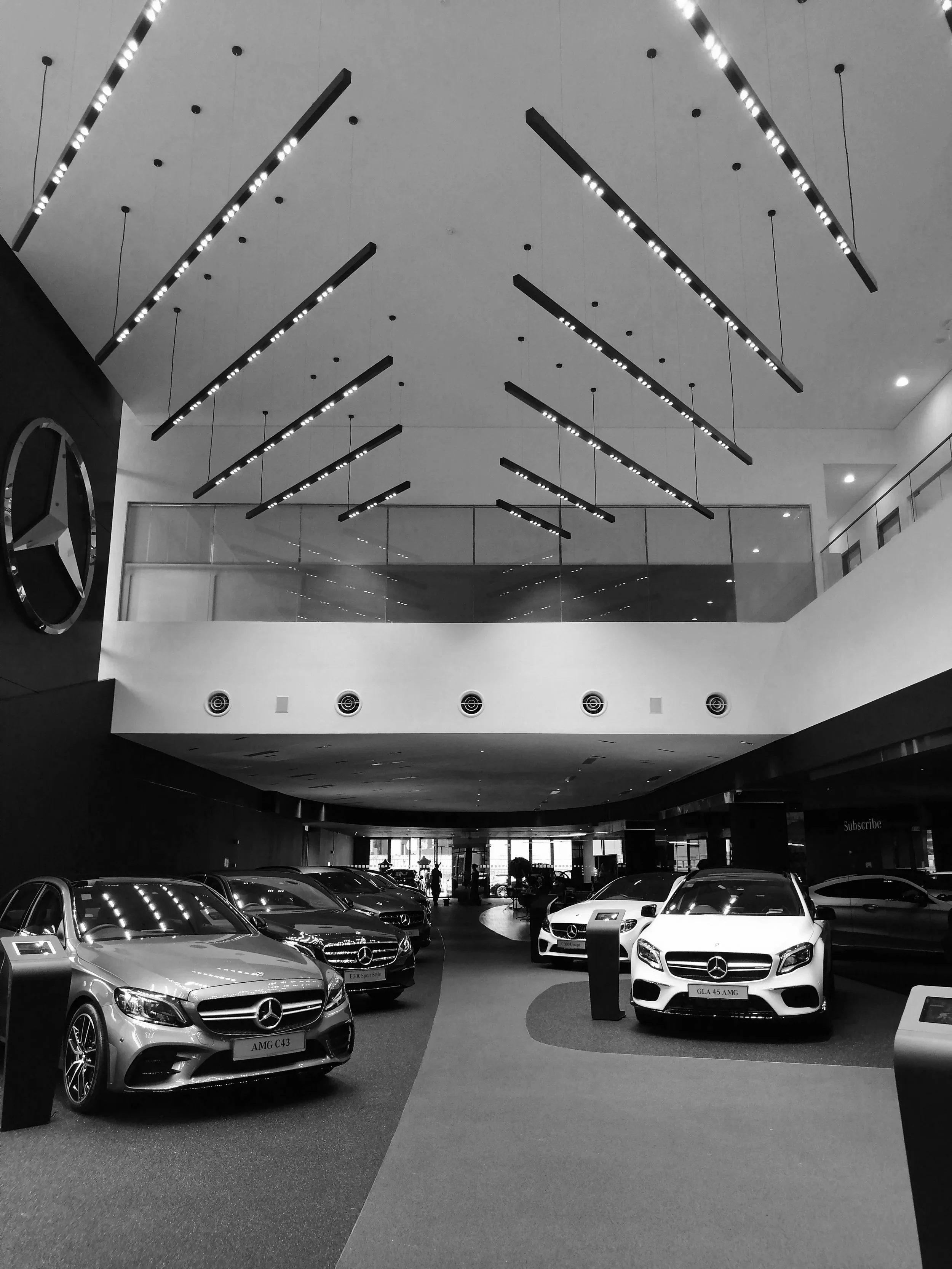 Interior of a Mercedes-Benz car dealership showcasing luxury vehicles, including models labeled AMG C43, GLA 45 AMG, and E 300 Sport.
