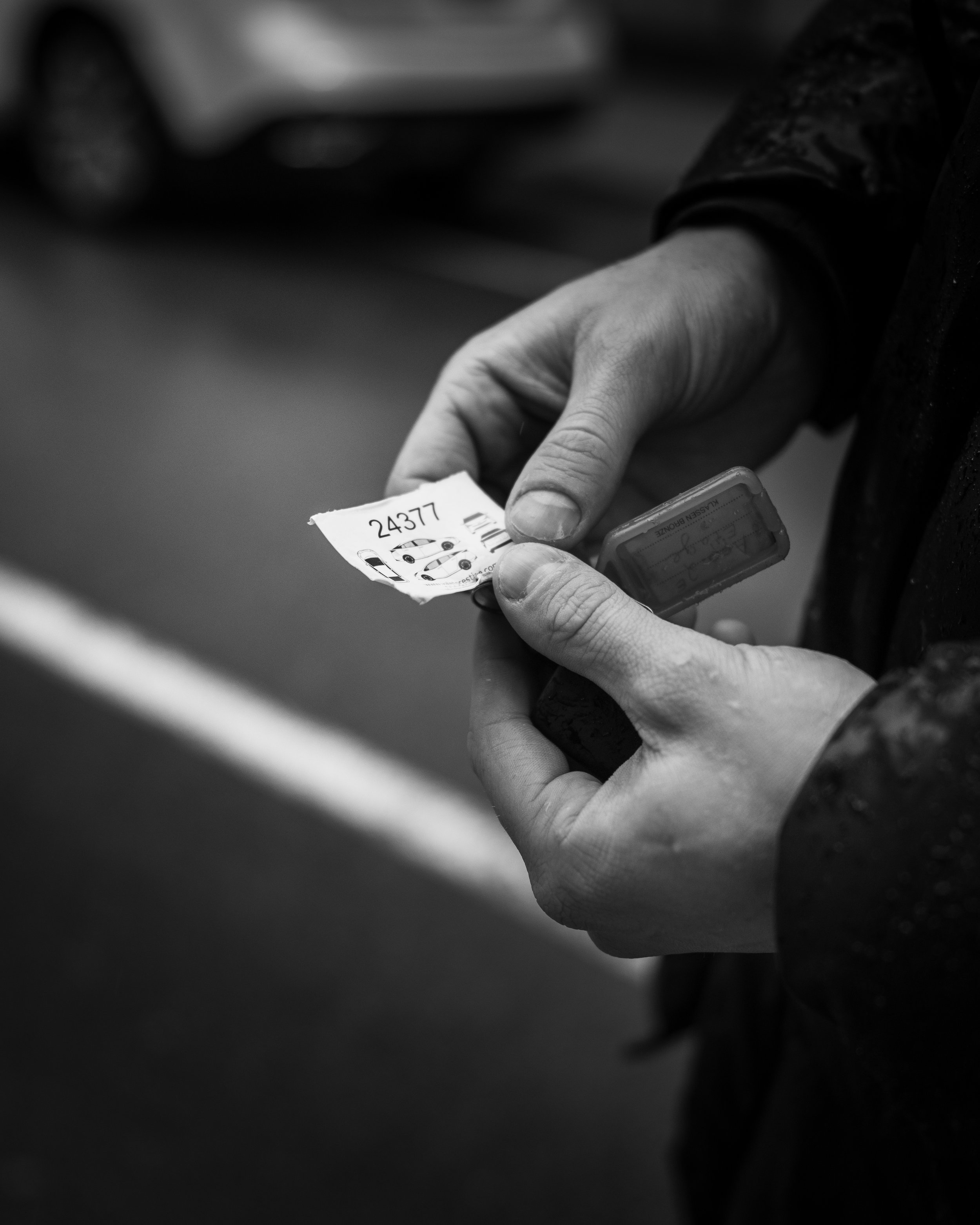Close-up of a person's hand holding a small torn piece of paper with the number '24377' and a car illustration, against a blurred background.