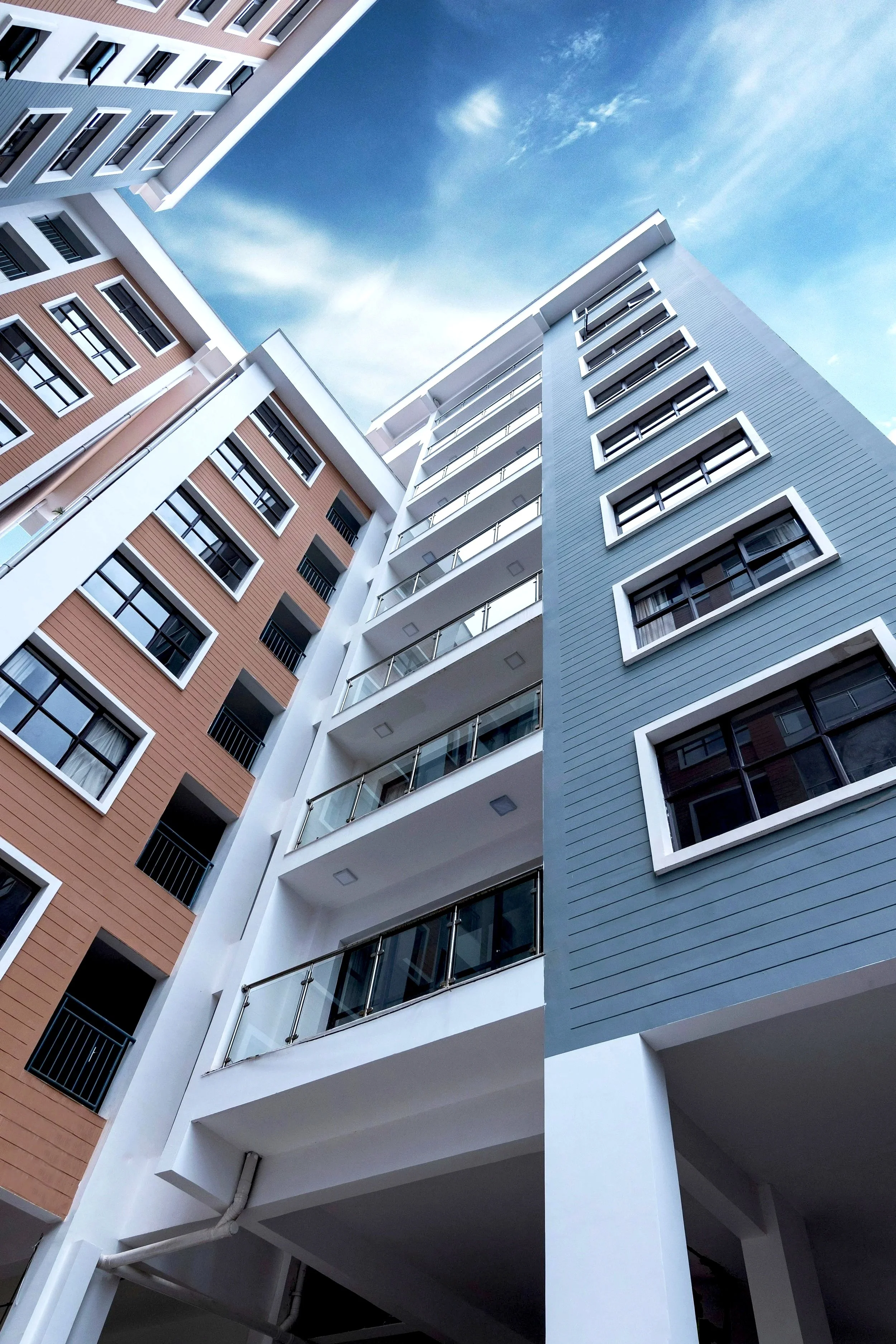 Low-angle view of a modern multi-story apartment building with a blue sky background.