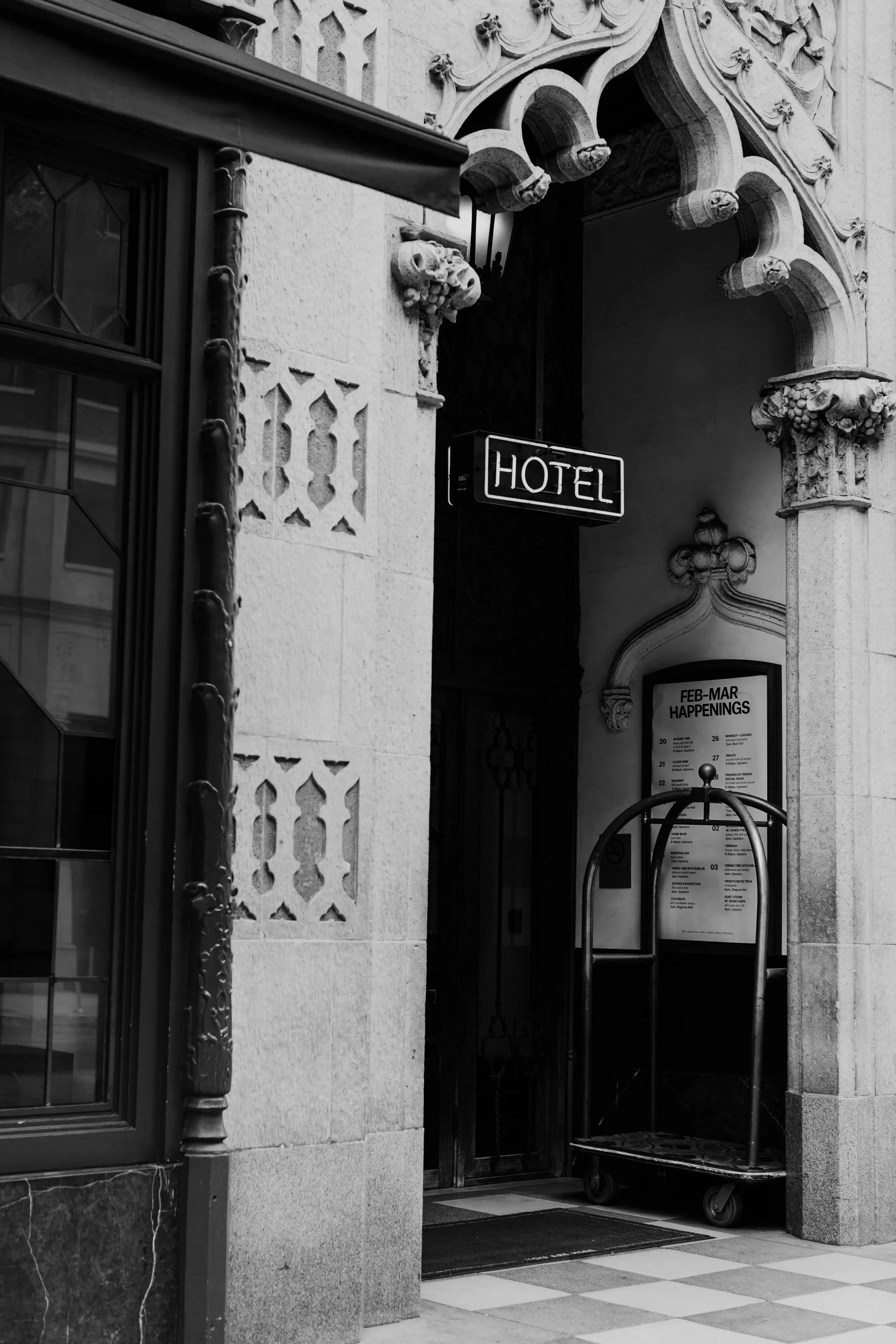 Photo of hotel entrance with ornate architectural details, a luggage cart, and a sign that reads 'HOTEL'