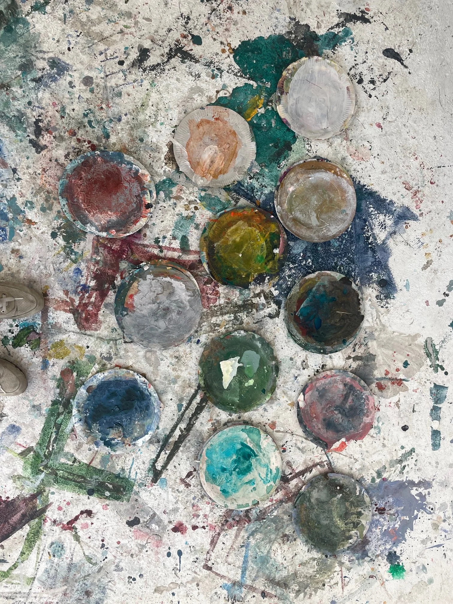 A messy tabletop with multiple used paint containers and splatters of dried paint in various colors.
