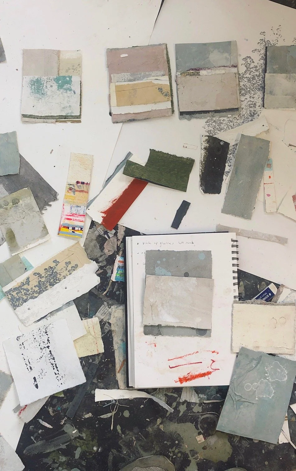A collection of paint color samples and swatches scattered across a work surface, with a notebook containing handwritten notes and paint swatches on its pages.