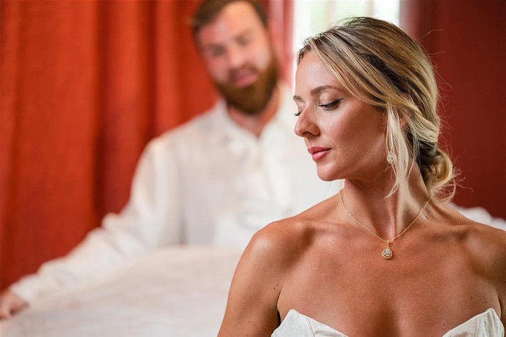 A bride with blonde hair wearing a necklace, looking down with a serene expression, in front of a The Bridal Steward.